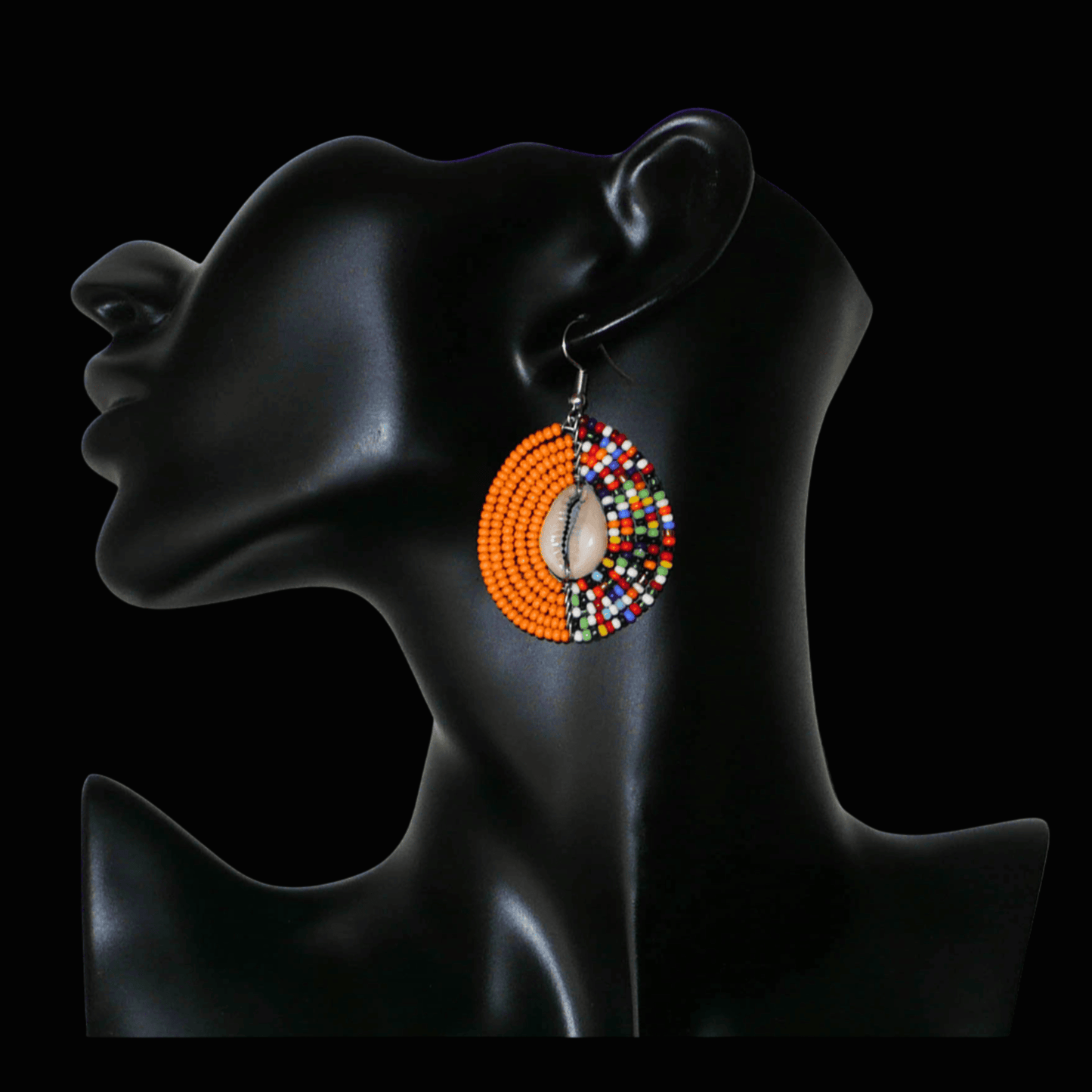 Boucles d'oreilles ethniques orange et multicolores fabriquées au Kenya composées de perles de rocaille et de coquillages cauris. De taille moyenne, elles mesurent 6 cm de long et 3,5 cm de large et se portent sur des oreilles percées.
