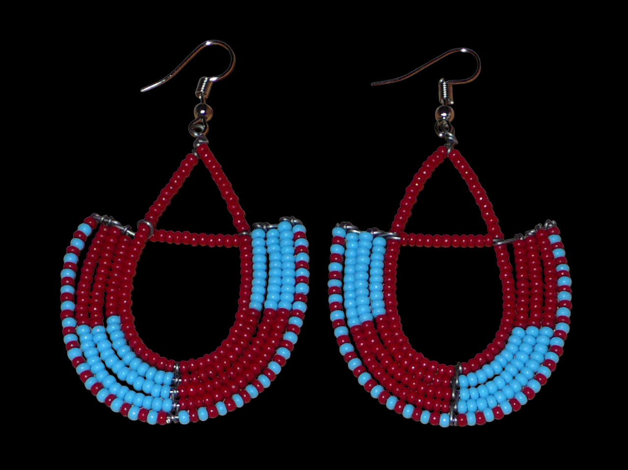 Boucles d'oreilles africaines Massai rouges et bleues composées de perles de rocaille glissées sur des structures géométriques en fils de fer montées en forme d'ancres. Ces boucles d'oreilles bicolores mesurent 7,5 cm de long et 4 cm de large et se portent avec des crochets en acier inoxydable.