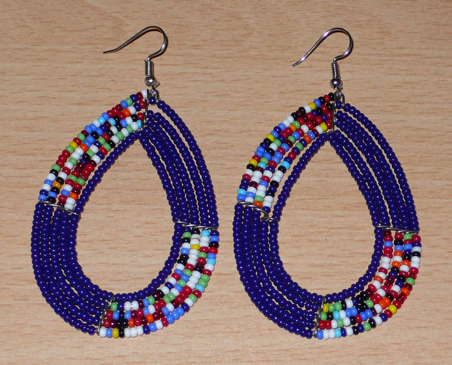 Longues boucles d'oreilles ethniques bleu marine et multicolores composées de perles de rocaille enfilées sur cinq rangées de fils de fer montés en forme de gouttes. Elles mesurent 8,5 cm de long et 4,5 cm de large, et se portent avec des crochets en acier inoxydable sur des oreilles percées.