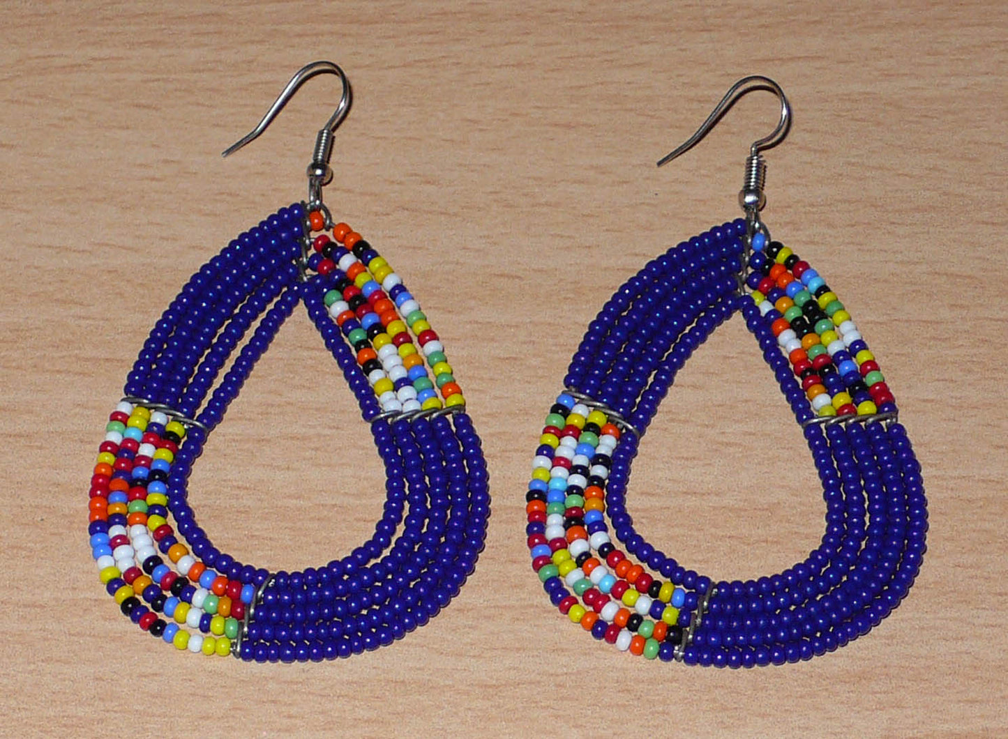 Boucles d'oreilles kenyanes composées de perles de rocaille bleu foncé et multicolores glissées sur cinq rangées de fils de fer montés en forme de triangles aux angles arrondis. Elles mesurent 8 cm de long et 4,5 cm de large, et se portent avec des crochets en acier inoxydable sur des oreilles percées.