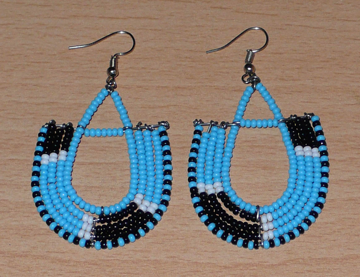 Boucles d'oreilles ethniques tricolores en forme d'ancres composées de perles bleues, noires et blanches. Elles mesurent 7 cm de long et 4 cm de large et se portent sur des oreilles percées.