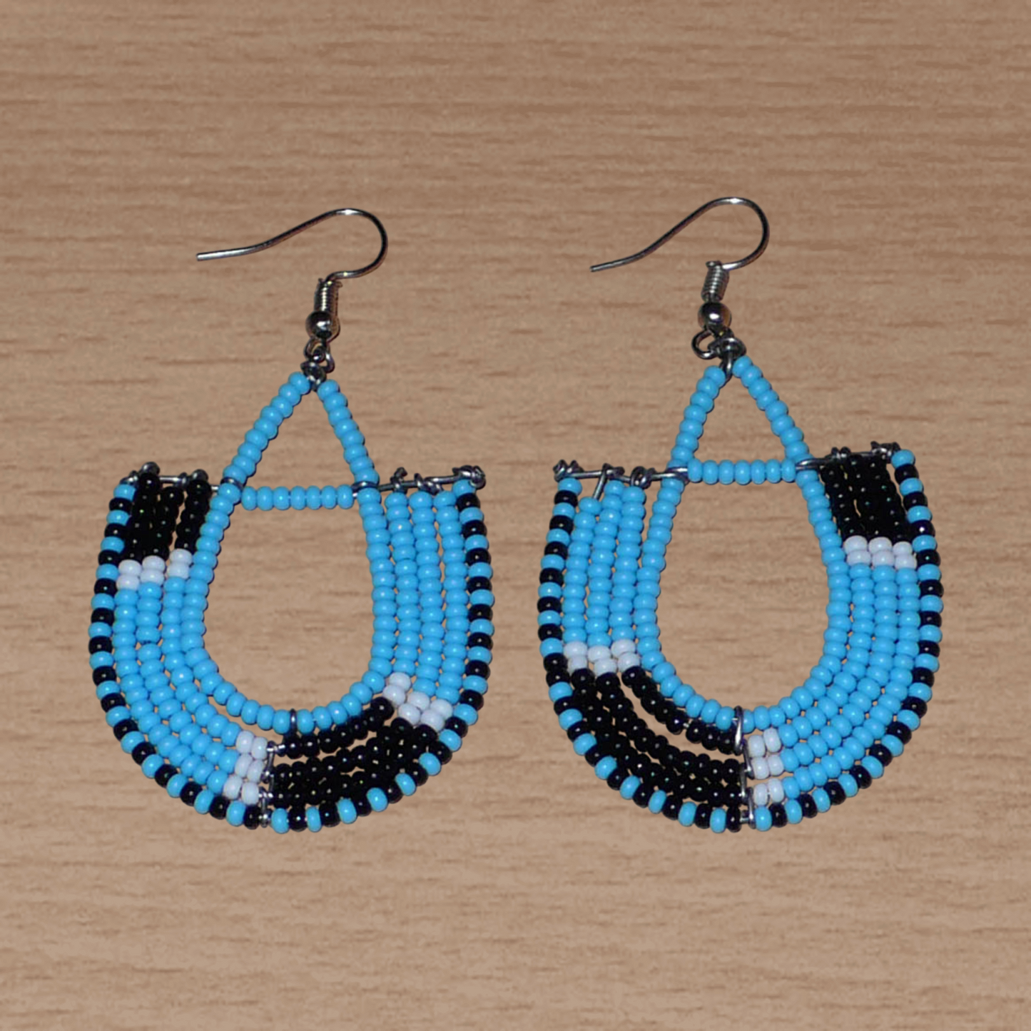 Boucles d'oreilles ethniques tricolores en forme d'ancres composées de perles bleues, noires et blanches. Elles mesurent 7 cm de long et 4 cm de large et se portent sur des oreilles percées.
