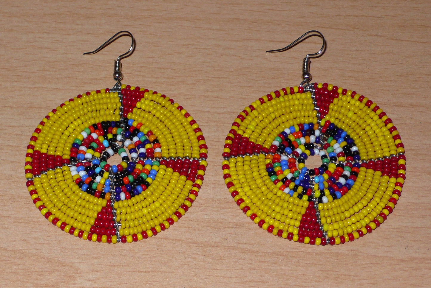 Boucles d'oreilles ethniques kenyanes en perles de rocaille principalement jaunes, puis rouges et multicolores enfilées sur des structures circulaires en fils de fer. Elles mesurent 7.5 cm de long et se portent sur des oreilles percées.