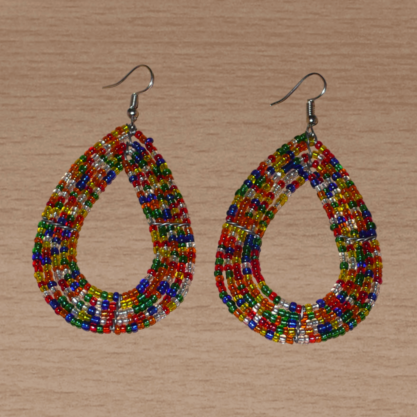 Boucles d'oreilles ethniques composées d'un mélange de perles de rocaille translucides multicolores enfilées sur cinq rangées de fils de fer montés en forme de gouttes. Elles mesurent 8 cm de long et 4,5 cm de large, et se portent avec des crochets sur des oreilles percées.