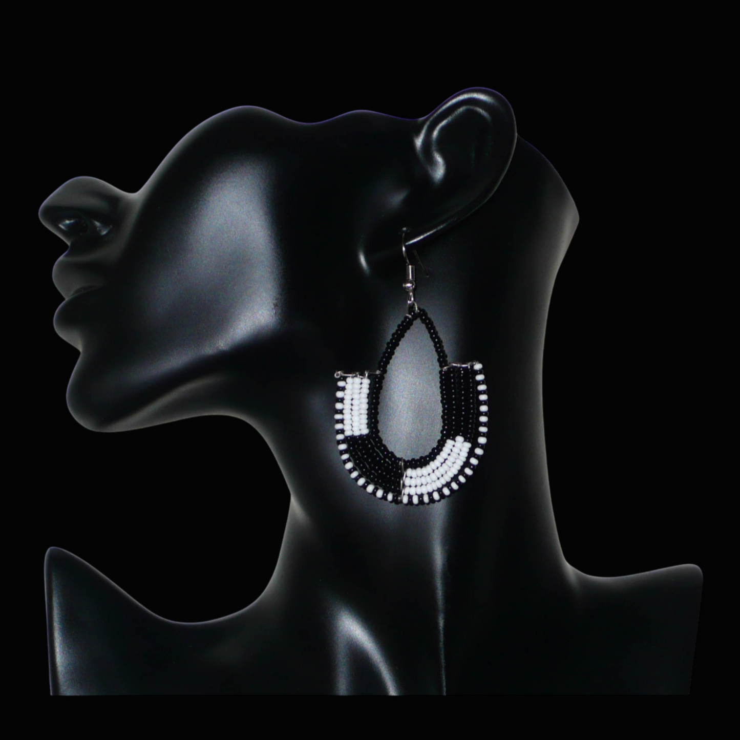 Boucles d'oreilles ethniques bicolores en forme d'ancres composées de perles de rocaille noires et blanches glissées sur des structures géométriques en fils de fer. De taille moyenne, ces boucles d'oreilles aux accents afro chic mesurent 7 cm de long et 4 cm de large ; elles se portent avec des crochets en acier inoxydable sur des oreilles percées.