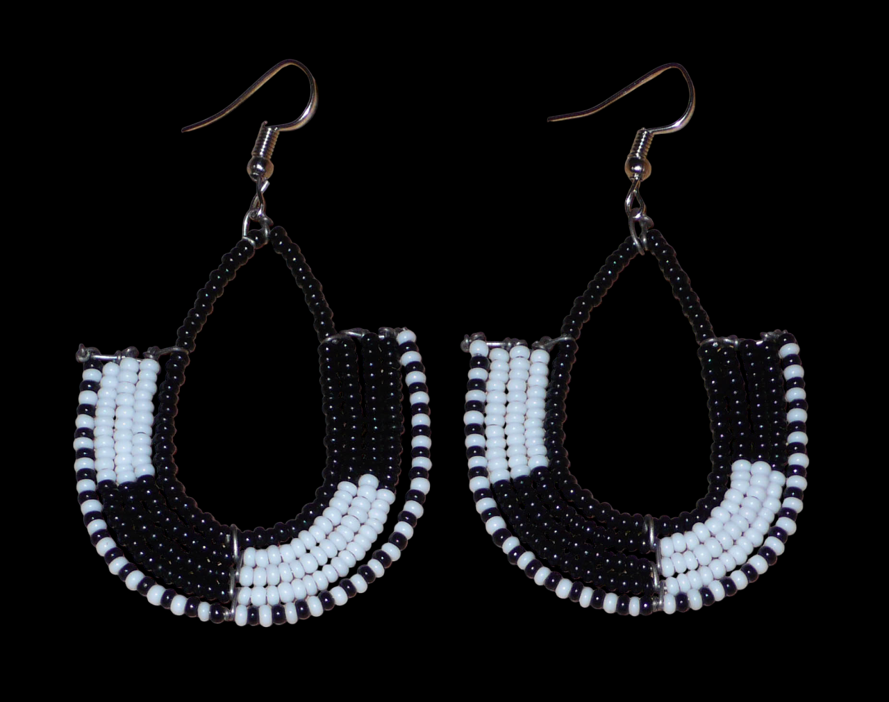Boucles d'oreilles ethniques bicolores en forme d'ancres composées de perles de rocaille noires et blanches glissées sur des structures géométriques en fils de fer. De taille moyenne, ces boucles d'oreilles aux accents afro chic mesurent 7 cm de long et 4 cm de large ; elles se portent avec des crochets en acier inoxydable sur des oreilles percées.