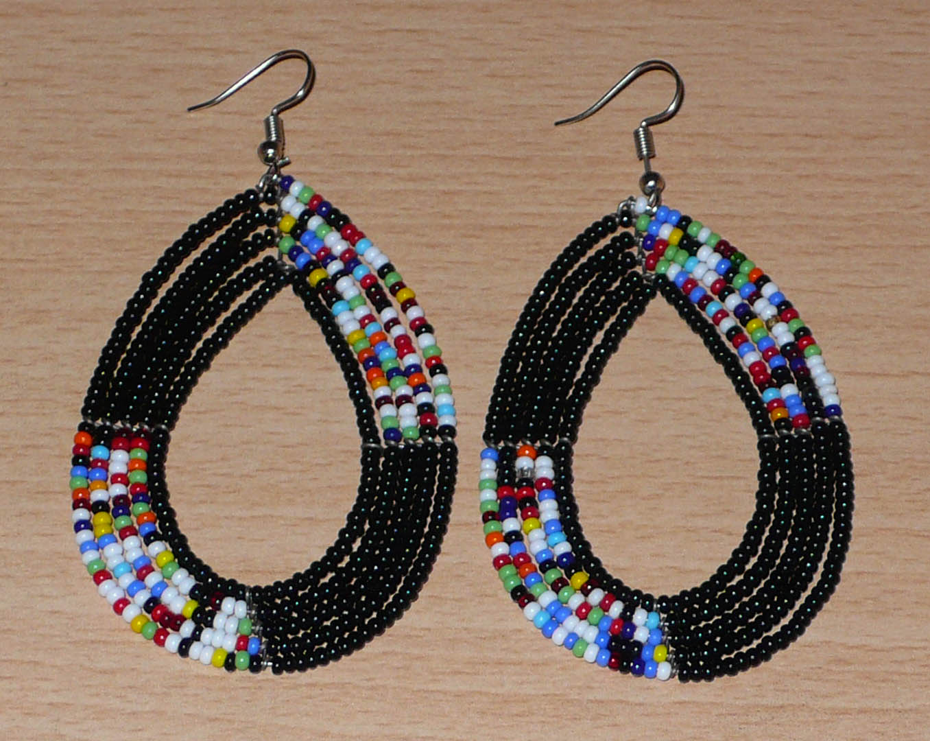 Longues boucles d'oreilles kenyanes en perles de rocaille noires et multicolores glissées sur cinq rangées de fils de fer montés en forme de gouttes. Elles mesurent 8,5 cm de long et 5 cm de large et se portent avec des crochets en acier inoxydable sur des oreilles percées.