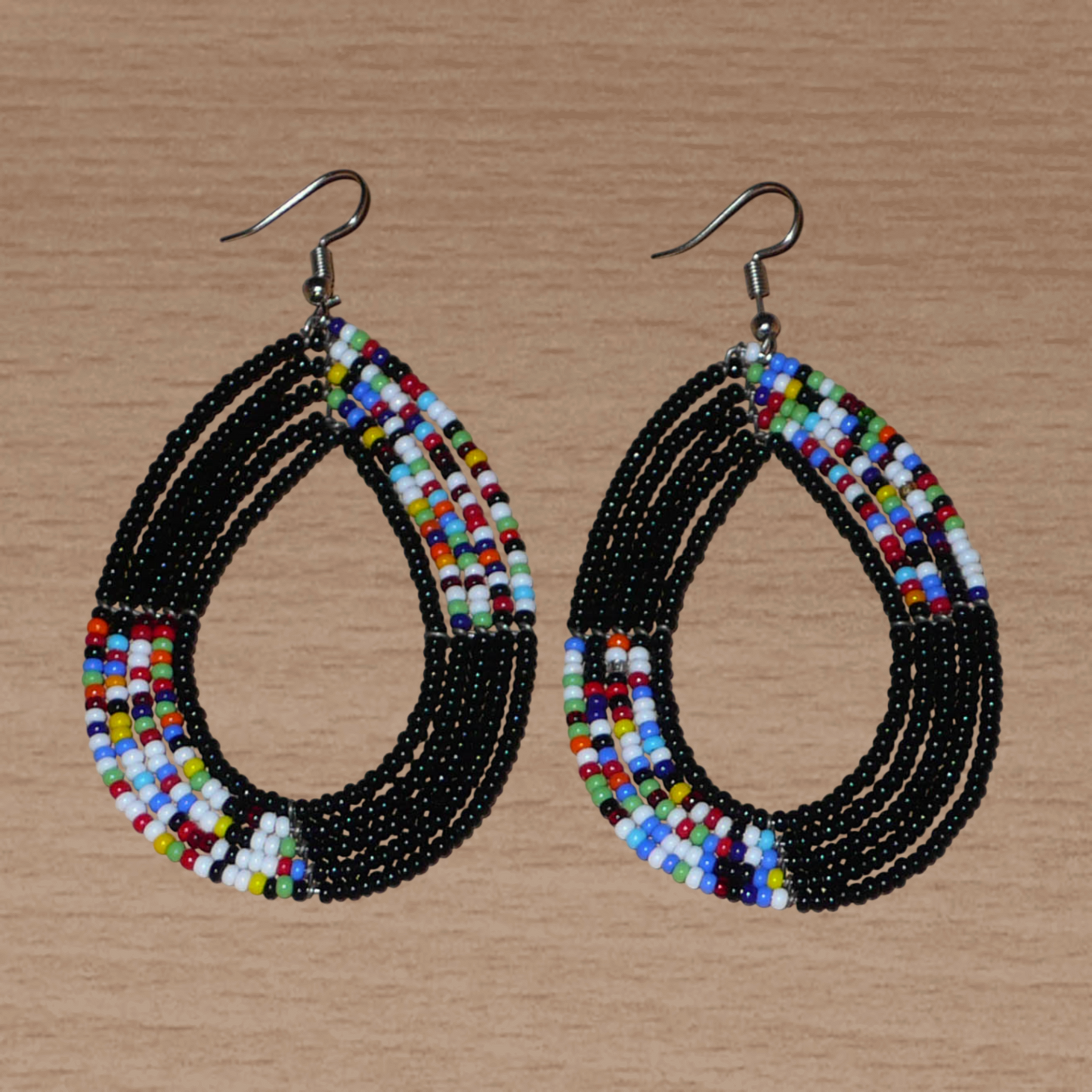Longues boucles d'oreilles kenyanes en perles de rocaille noires et multicolores glissées sur cinq rangées de fils de fer montés en forme de gouttes. Elles mesurent 8,5 cm de long et 5 cm de large et se portent avec des crochets en acier inoxydable sur des oreilles percées.
