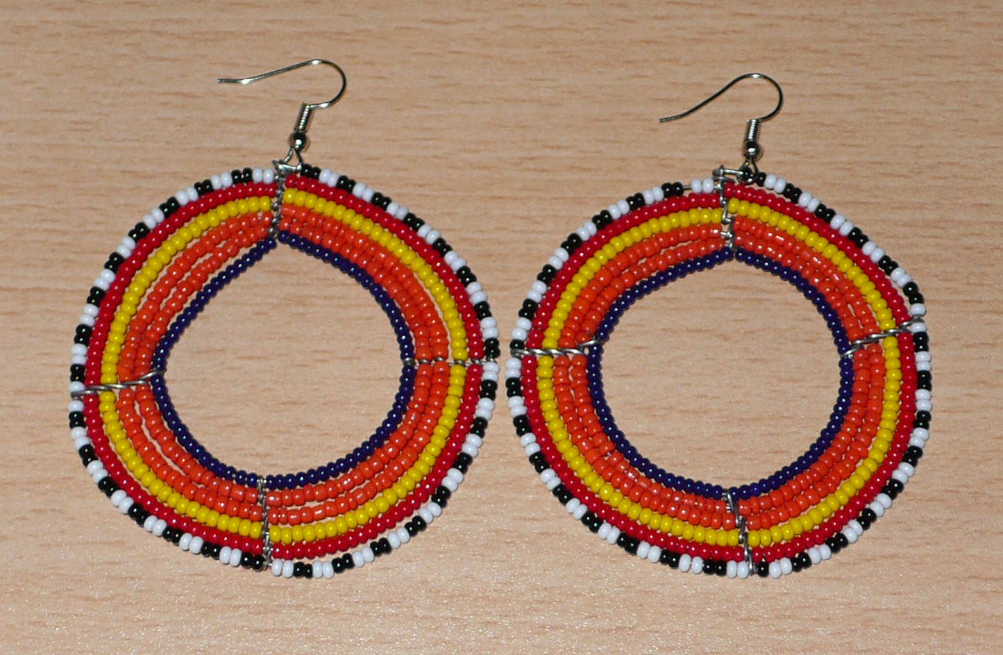 Boucles d'oreilles ethniques rondes composées de perles de rocaille principalement orange. Elles mesurent 8 cm de long et 6,5 cm de large et se portent sur des oreilles percées.