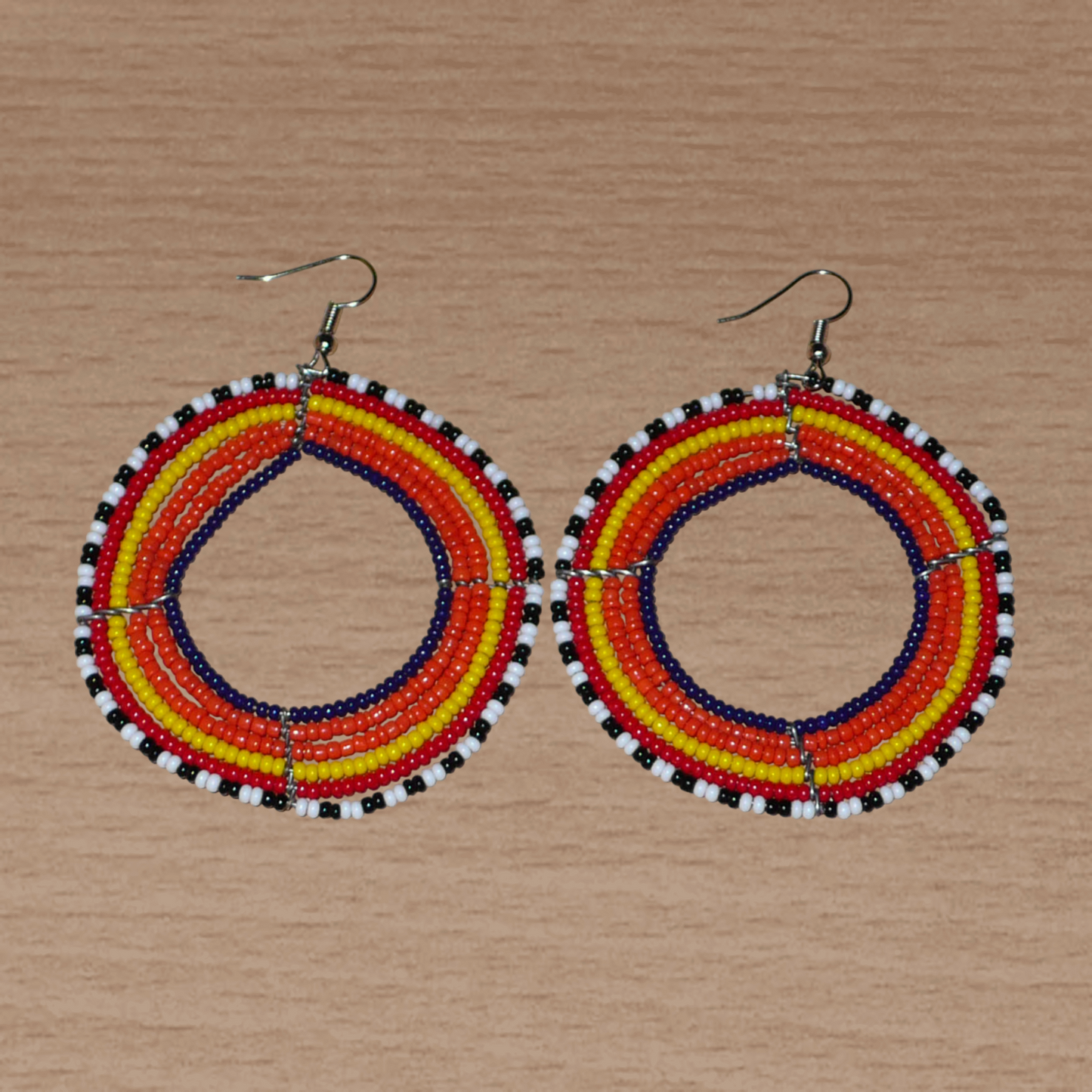 Boucles d'oreilles ethniques rondes composées de perles de rocaille principalement orange. Elles mesurent 8 cm de long et 6,5 cm de large et se portent sur des oreilles percées.