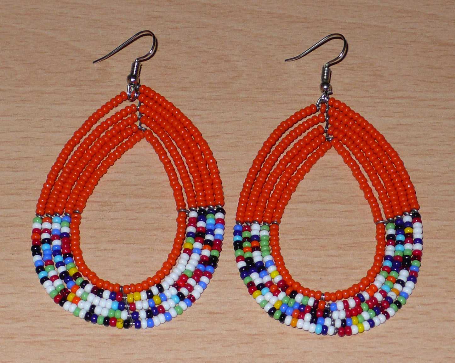 Longues boucles d'oreilles kenyanes en forme de gouttes composées de perles de rocaille orange et multicolores. Elles mesurent 8,5 cm de long et 4,5 cm de large et se portent avec des crochets en acier inoxydable sur des oreilles percées.