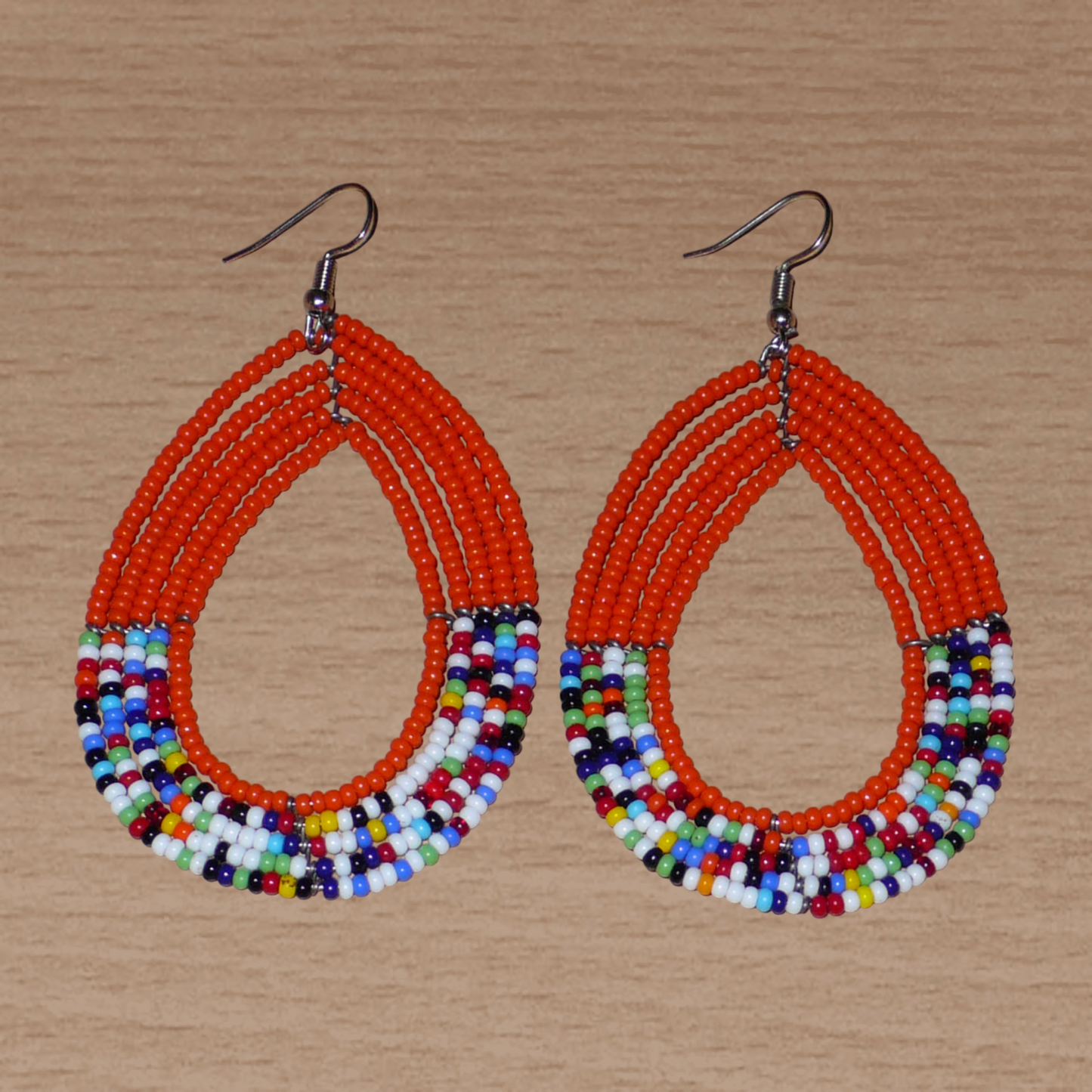 Longues boucles d'oreilles kenyanes en forme de gouttes composées de perles de rocaille orange et multicolores. Elles mesurent 8,5 cm de long et 4,5 cm de large et se portent avec des crochets en acier inoxydable sur des oreilles percées.