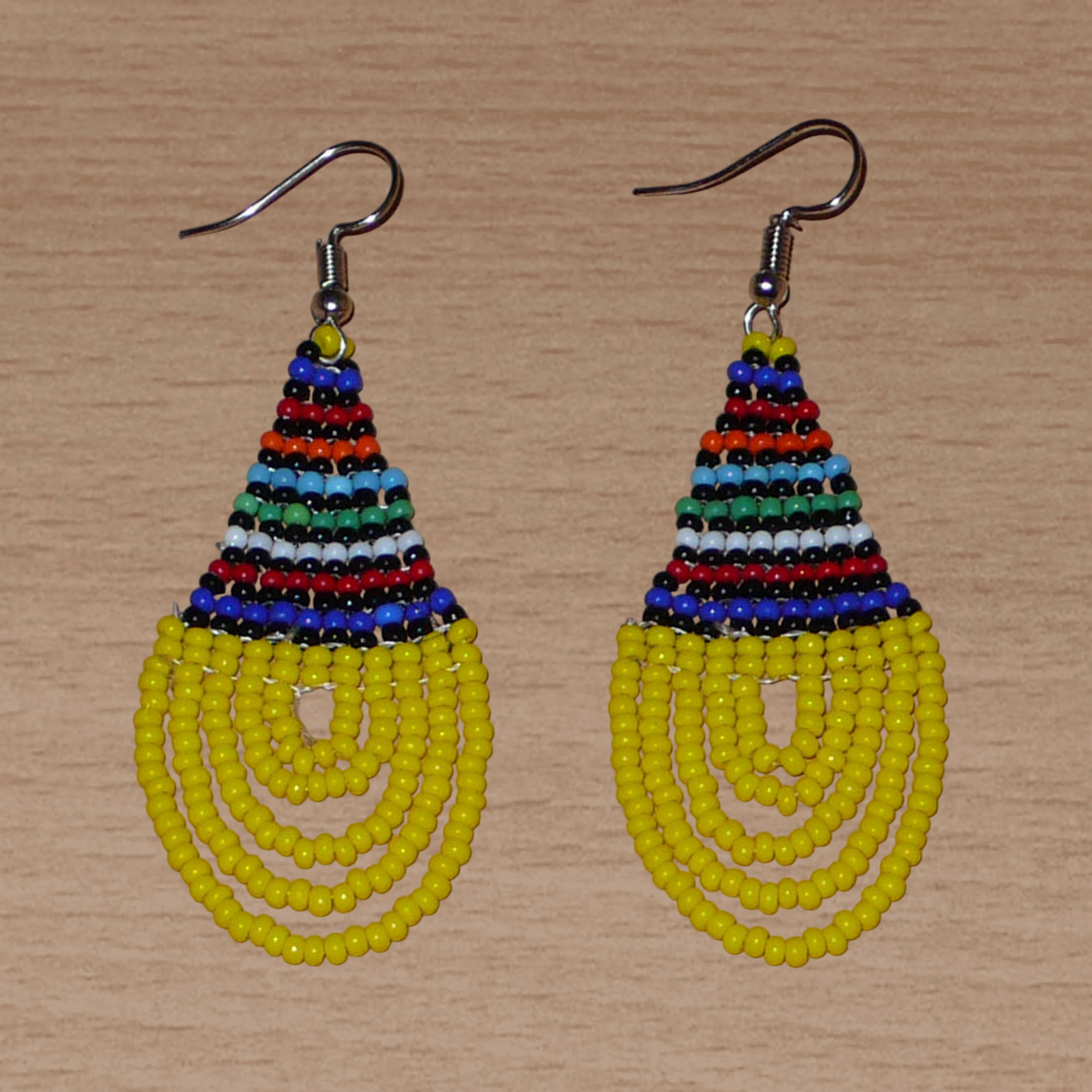 Boucles d'oreilles ethniques jaunes et multicolores composées d'un tissage en forme de gouttes de perles de rocaille. De taille moyenne et légère à porter, elles mesurent 7 cm de long et 2,5 cm de large et se portent avec des crochets en acier inoxydable sur des oreilles percées.