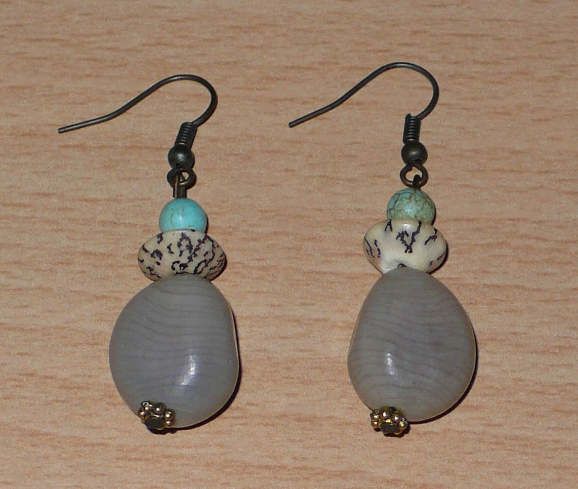Boucles d'oreilles exotiques composées de perles et de graines de caniques grises. De taille moyenne, elles mesurent 5 cm de long et 1,5 cm de large, et se portent sur des oreilles percées.