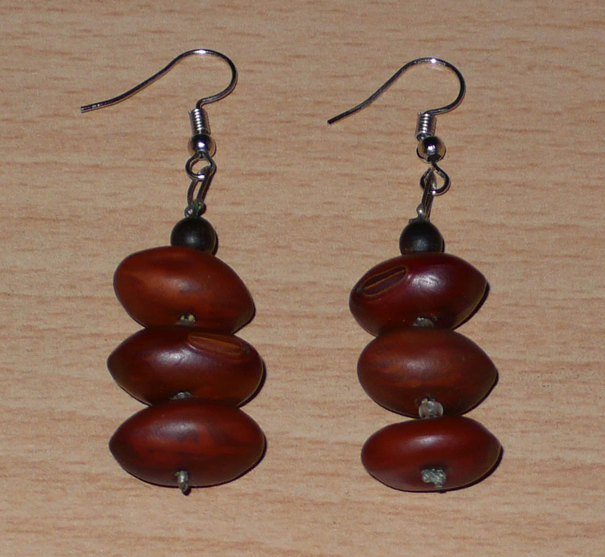 Boucles d'oreilles afro-caribéennes composées de graines organiques issues de la forêt tropicale et de perles de rocailles translucides. De taille moyenne, elles mesurent 6 cm de long et 2 cm de large, et se portent avec des crochets en acier inoxydable sur des oreilles percées.