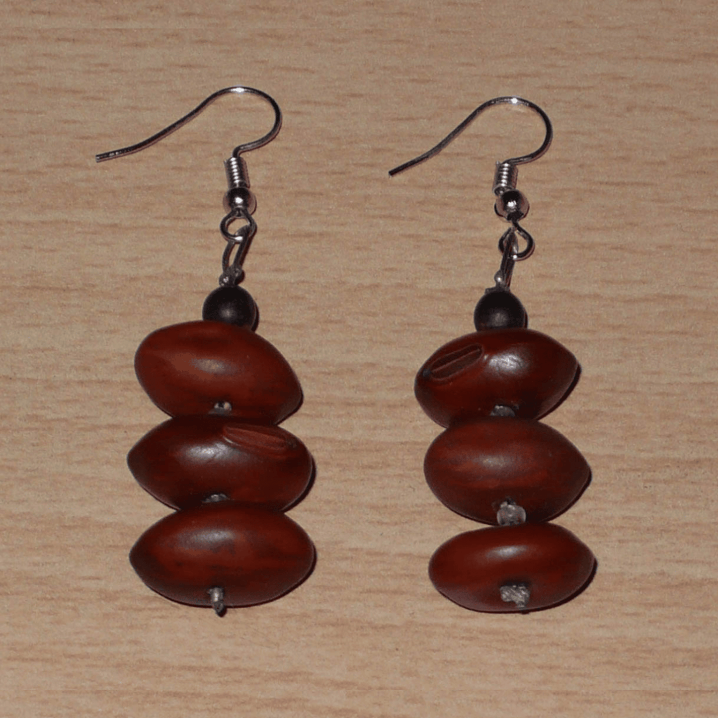 Boucles d'oreilles afro-caribéennes composées de graines organiques issues de la forêt tropicale et de perles de rocailles translucides. De taille moyenne, elles mesurent 6 cm de long et 2 cm de large, et se portent avec des crochets en acier inoxydable sur des oreilles percées.