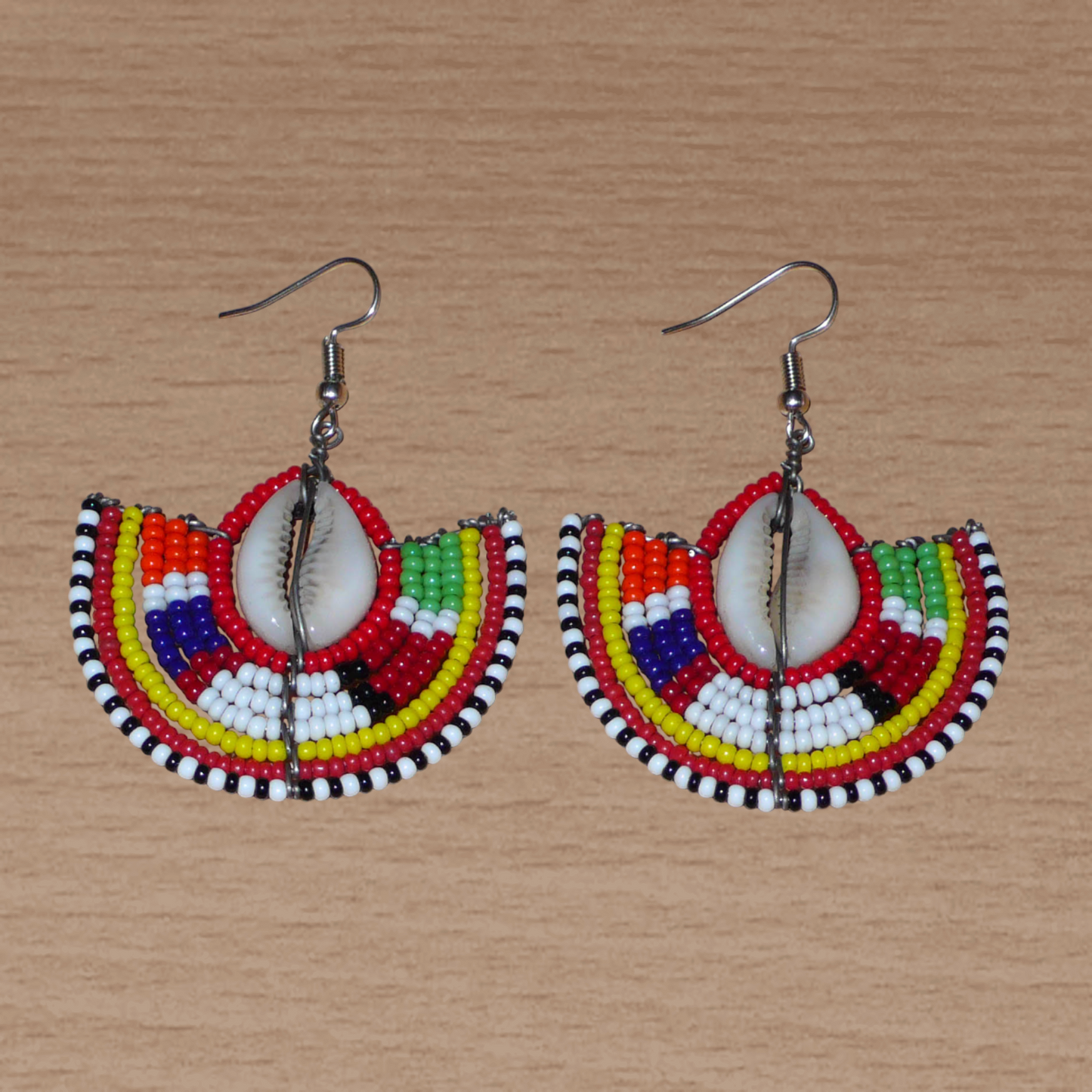 Ajoutez une touche exotique à votre style avec cette jolie paire de boucles d'oreilles africaines issues de l'artisanat traditionnel Massai. Ces boucles d'oreilles ethniques chic se composent de perles de rocaille rouges et multicolores et de coquillages cauris. De taille moyenne, elles mesurent 6 cm de long et 4.5 cm de large, et se portent avec des crochets en acier inoxydable sur des oreilles percées.