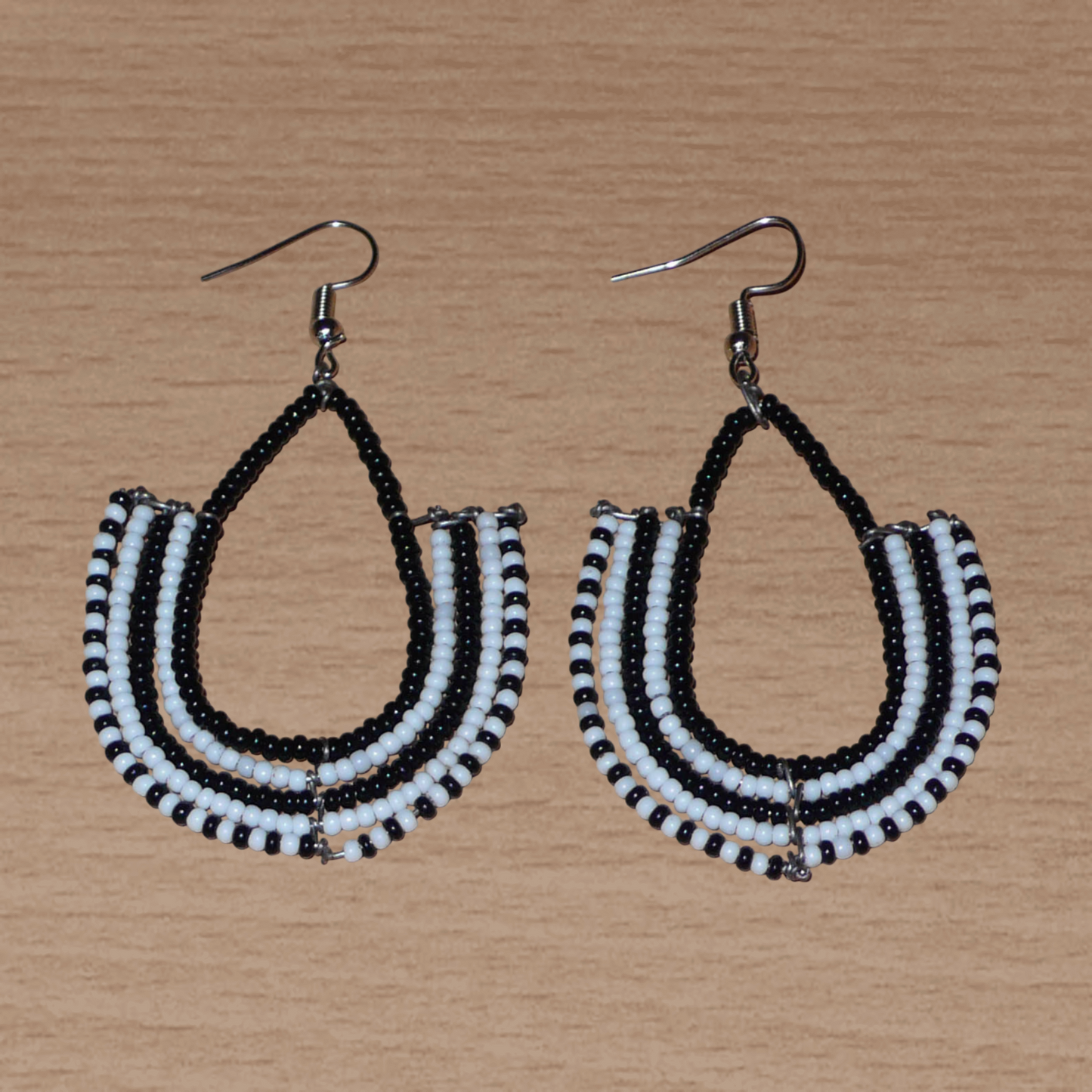 Boucles d'oreilles kenyanes Massai bicolores en forme d'ancres composées de perles de rocaille noires et blanches glissées sur des structures géométriques en fils de fer. De taille moyenne, ces boucles d'oreilles aux accents ethniques afro chic mesurent 7 cm de long et 4 cm de large ; elles se portent avec des crochets en acier inoxydable sur des oreilles percées.