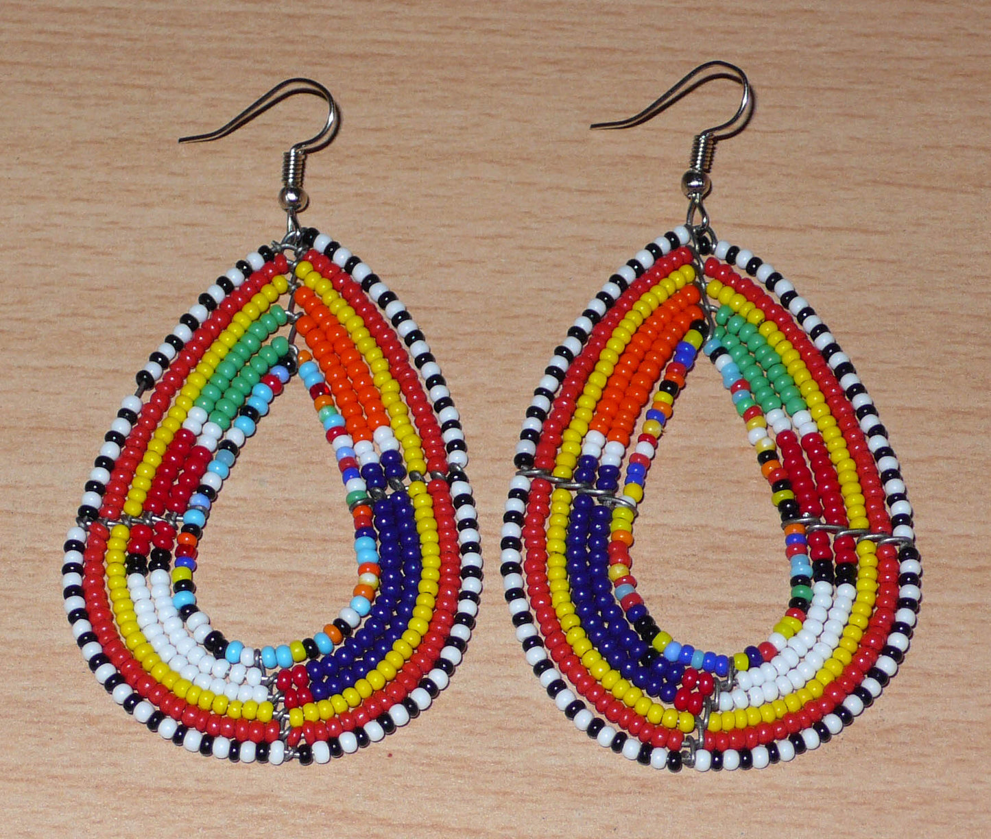 Ajoutez de la couleur à votre look avec ces longues boucles d'oreilles africaines à motifs ethniques traditionnels Massai. Confectionnées selon la tradition artisanale kenyane, elles sont composées de perles de rocaille multicolores glissées sur six rangées de fils de fer montés en forme de gouttes. Ces boucles d'oreilles mesurent 8 cm de long et 4.5 cm de large ; elles se portent avec des crochets en acier inoxydable sur des oreilles percées.
