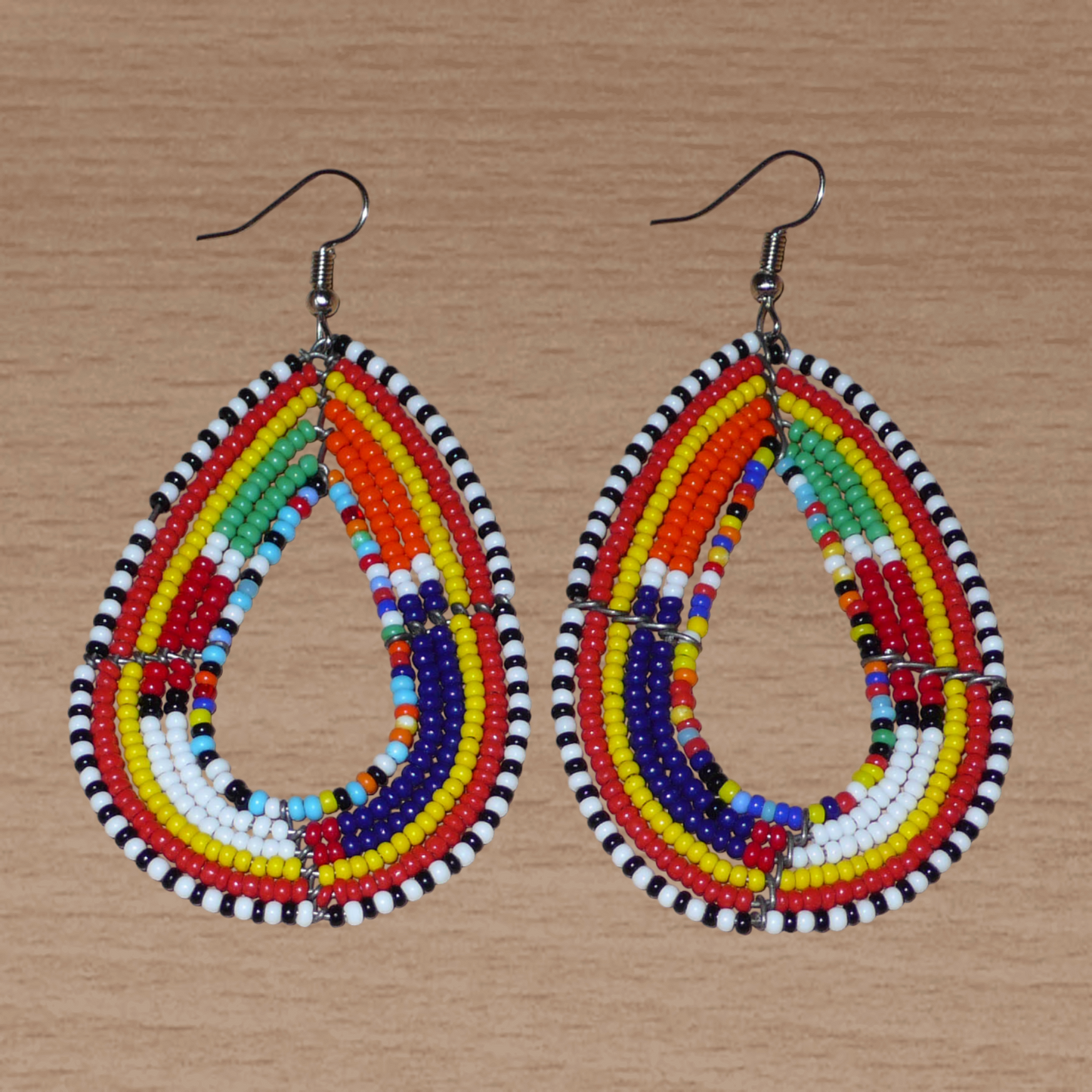 Ajoutez de la couleur à votre look avec ces longues boucles d'oreilles africaines à motifs ethniques traditionnels Massai. Confectionnées selon la tradition artisanale kenyane, elles sont composées de perles de rocaille multicolores glissées sur six rangées de fils de fer montés en forme de gouttes. Ces boucles d'oreilles mesurent 8 cm de long et 4.5 cm de large ; elles se portent avec des crochets en acier inoxydable sur des oreilles percées.