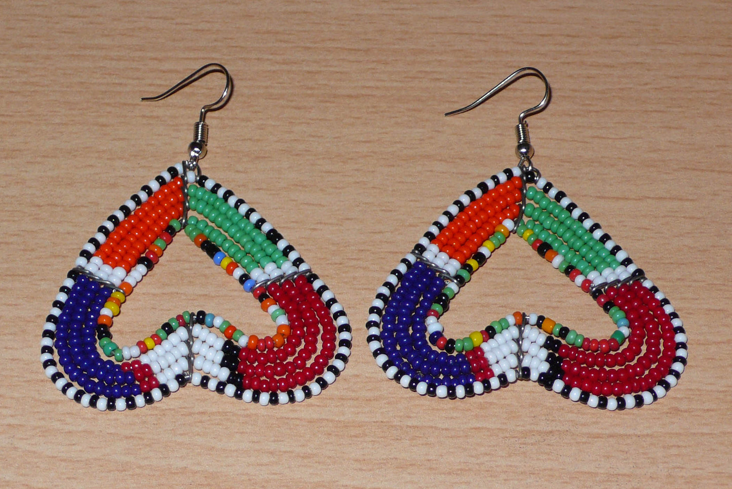 Boucles d'oreilles kenyanes Massai de fabrication artisanale se composant de perles de rocaille multicolores glissées sur cinq rangées de fils de fer montés en forme de cœurs inversés.
Cette paire de boucles d'oreilles de taille moyenne mesure 6.5 cm de long et 5 cm de large ; elle se porte avec des crochets en acier inoxydable sur des oreilles percées.
