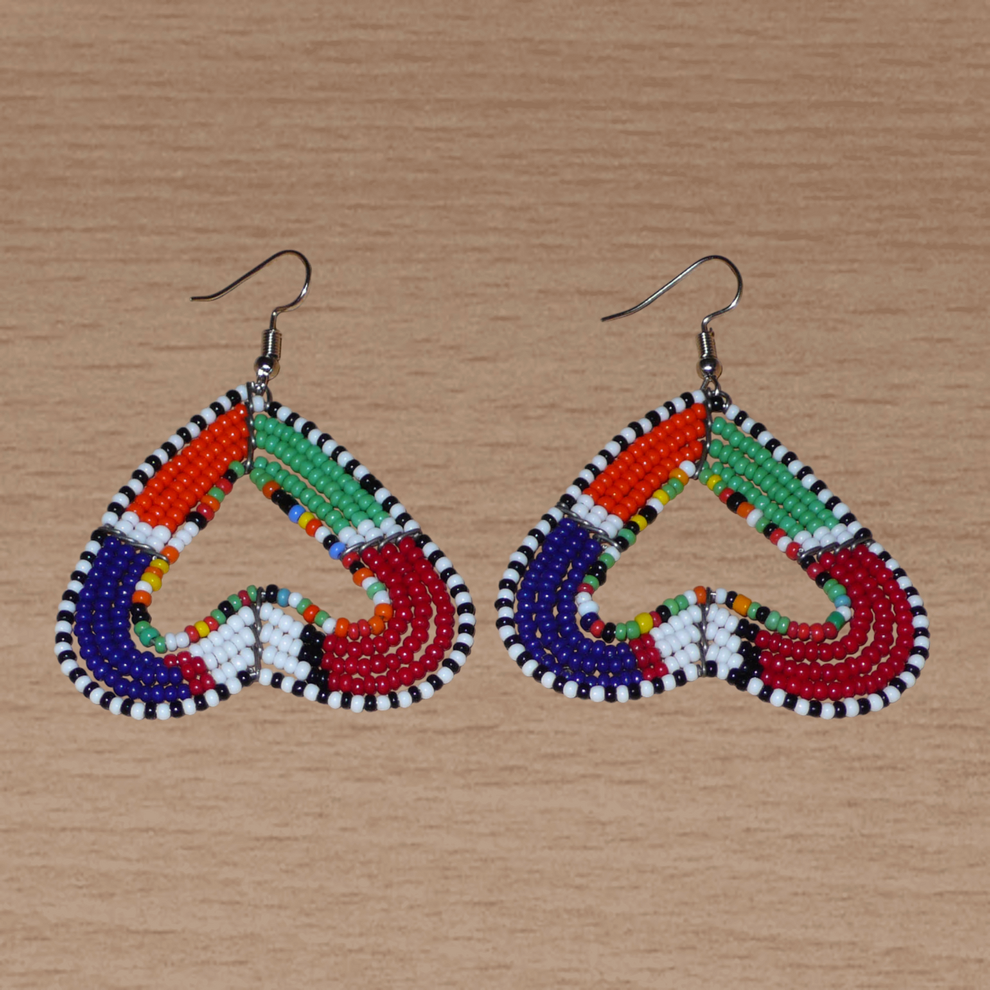 Boucles d'oreilles kenyanes Massai de fabrication artisanale se composant de perles de rocaille multicolores glissées sur cinq rangées de fils de fer montés en forme de cœurs inversés.
Cette paire de boucles d'oreilles de taille moyenne mesure 6.5 cm de long et 5 cm de large ; elle se porte avec des crochets en acier inoxydable sur des oreilles percées.