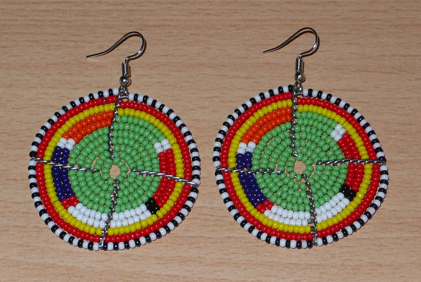 Boucles d'oreilles africaines Massai en perles de rocaille vertes et multicolores enfilées sur des structures circulaires en fils de fer. De taille moyenne, elles mesurent 6,5 cm de long et 4,5 cm de large ; elles se portent sur des oreilles percées.