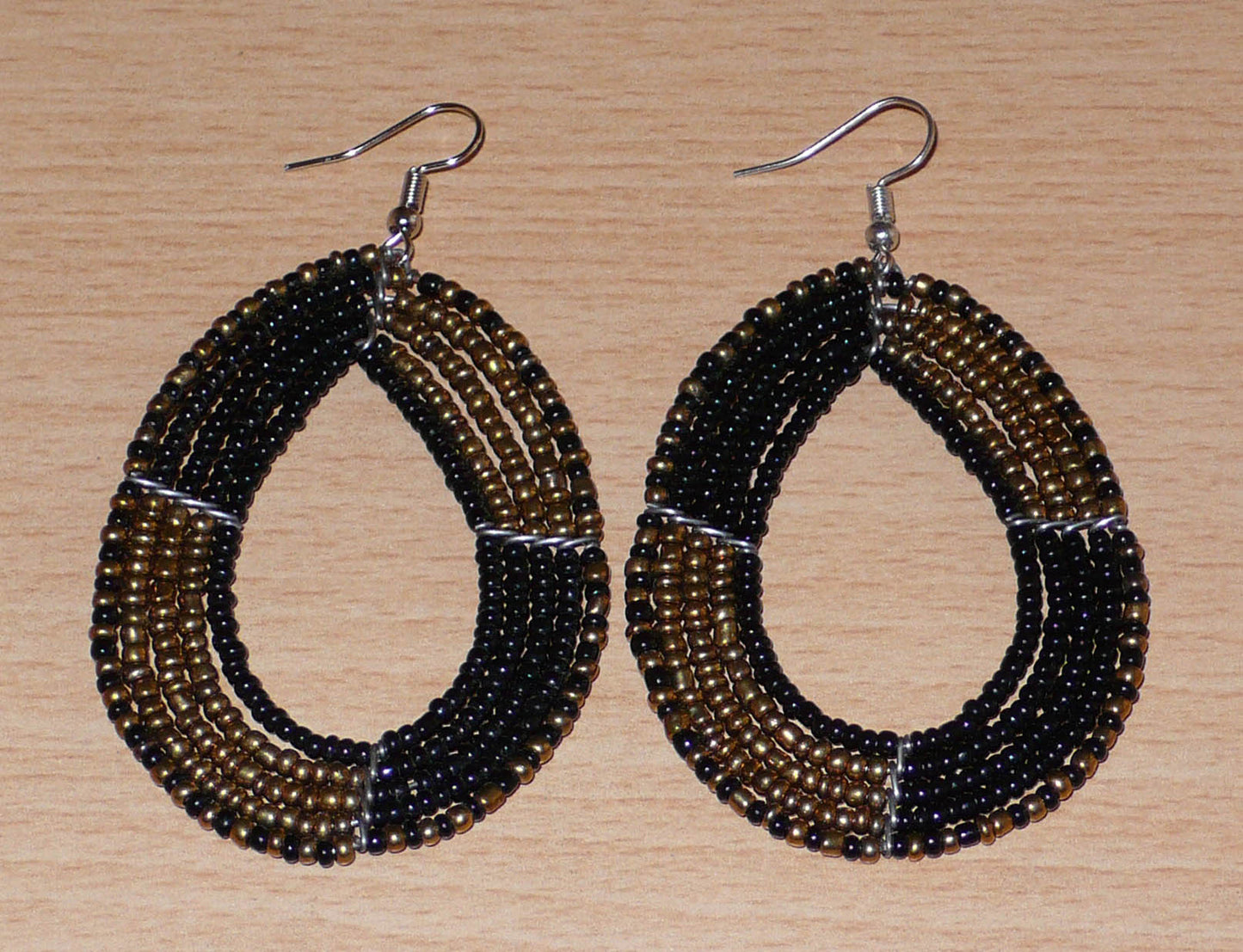 Boucles d'oreilles multi-rangs en perles de rocaille noires et dorées montées en forme de gouttes ; elles mesurent 8 cm de long et 4,5 cm de large, et se portent avec des crochets sur des oreilles percées.