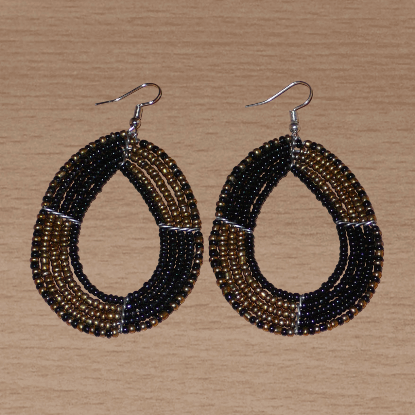 Boucles d'oreilles multi-rangs en perles de rocaille noires et dorées montées en forme de gouttes ; elles mesurent 8 cm de long et 4,5 cm de large, et se portent avec des crochets sur des oreilles percées.