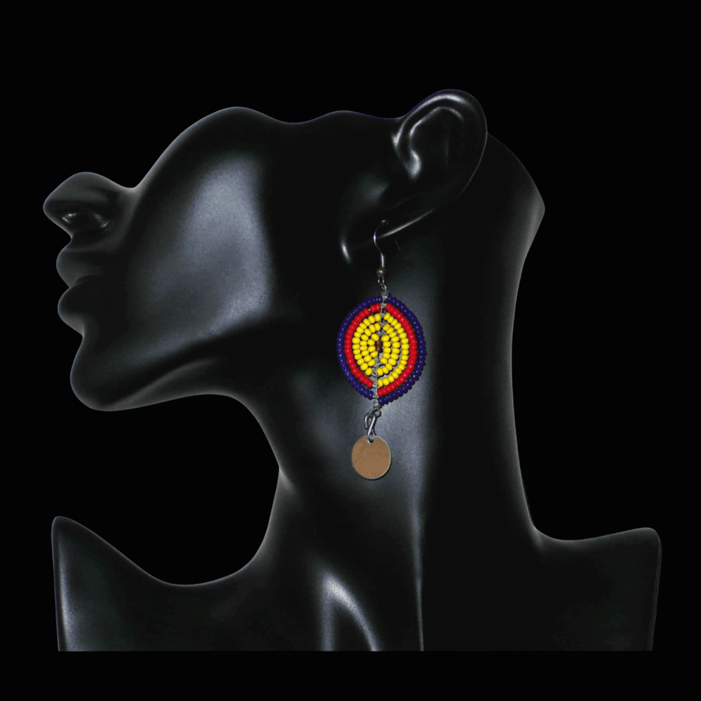 Boucles d'oreilles africaines en forme de boucliers Massai composées de perles de rocaille jaunes, rouges et bleu foncé ; elles se prolongent d'un disque métallique. Ces boucles d'oreilles mesurent 7 cm de long et 2,5 cm de large ; elles se portent sur des oreilles percées.