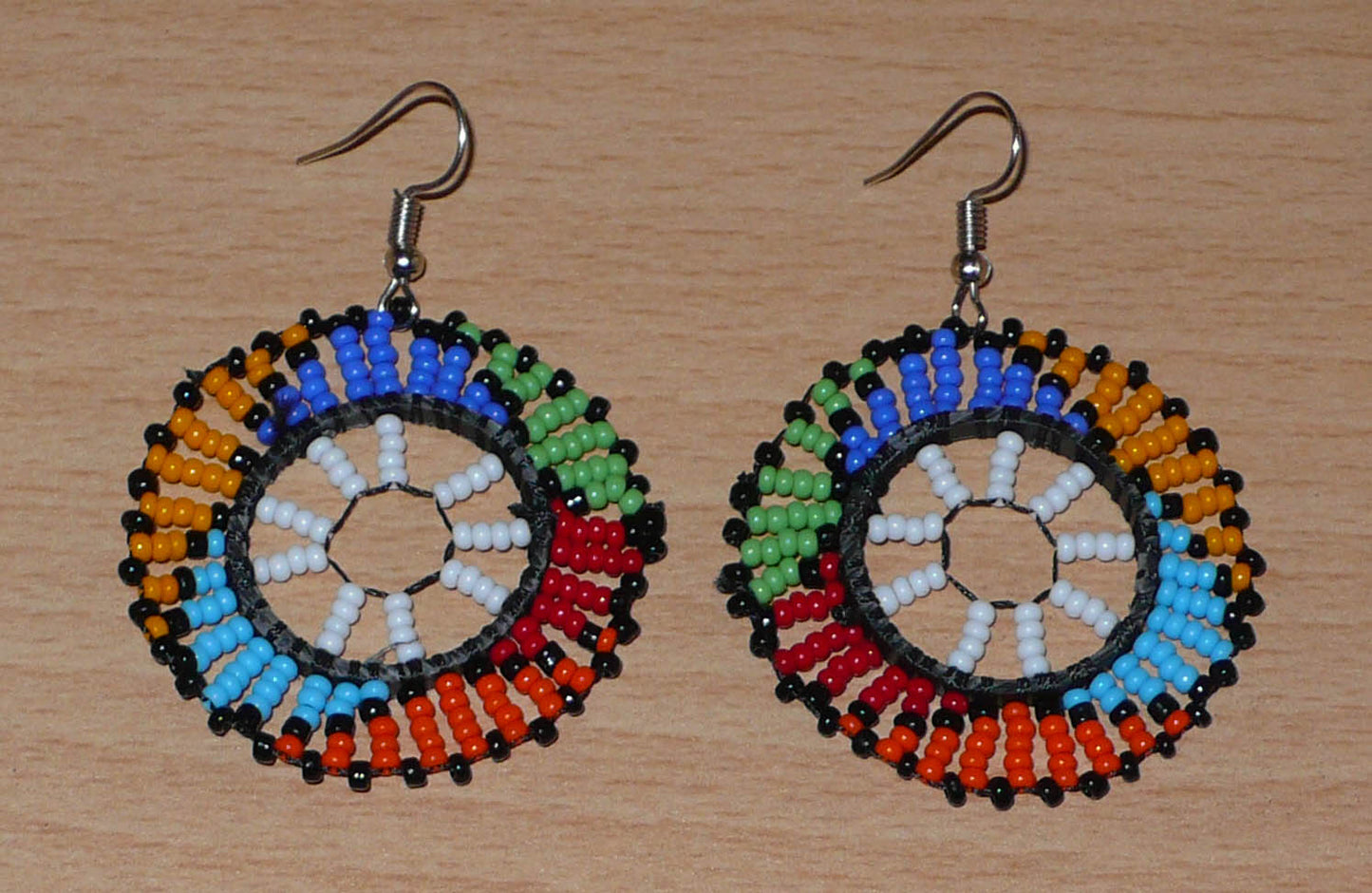 Boucles d'oreilles ethniques rondes à motifs sud-africains zoulous composées de perles de rocaille blanches et multicolores. De taille moyenne et légères à porter, elles mesurent 6 cm de long et 4 cm de large, et se portent sur des oreilles percées.