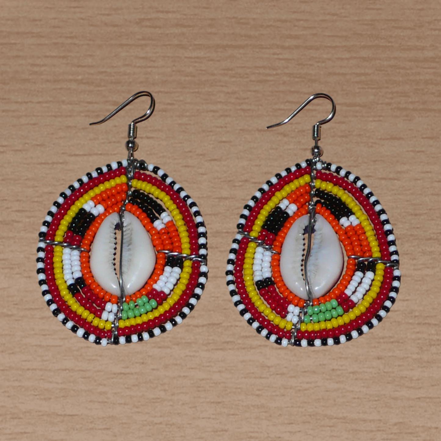 Boucles d'oreilles africaines en forme de boucliers Massai composées de perles et de coquillages. Elles mesurent 7 cm de long et 4 cm de large et se portent sur des oreilles percées.
