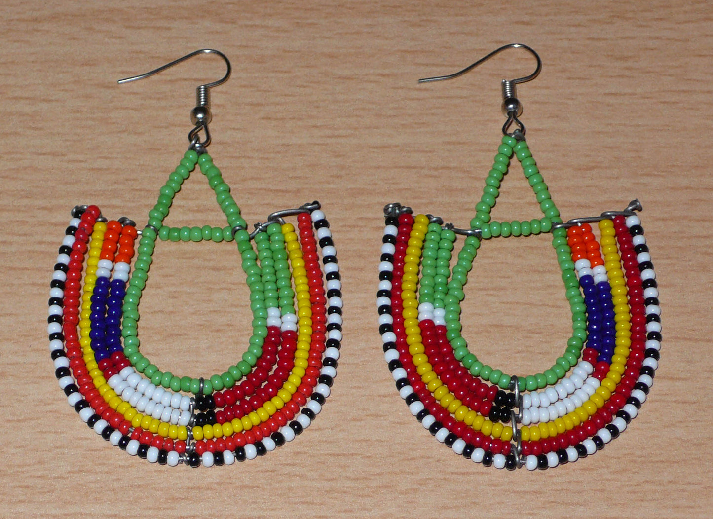 Cette paire de boucles d'oreilles africaines traditionnelles Massai riches en couleurs, de conception artisanale kenyane, apportera une touche tribale à votre look ! Elles se composent de perles de rocaille vertes et multicolores glissées sur des structures géométriques en fils de fer montés en forme d'ancres. Ces boucles d'oreilles mesurent 7.5 cm de long et 4.5 cm de large, et se portent avec des crochets en acier inoxydable sur des oreilles percées.