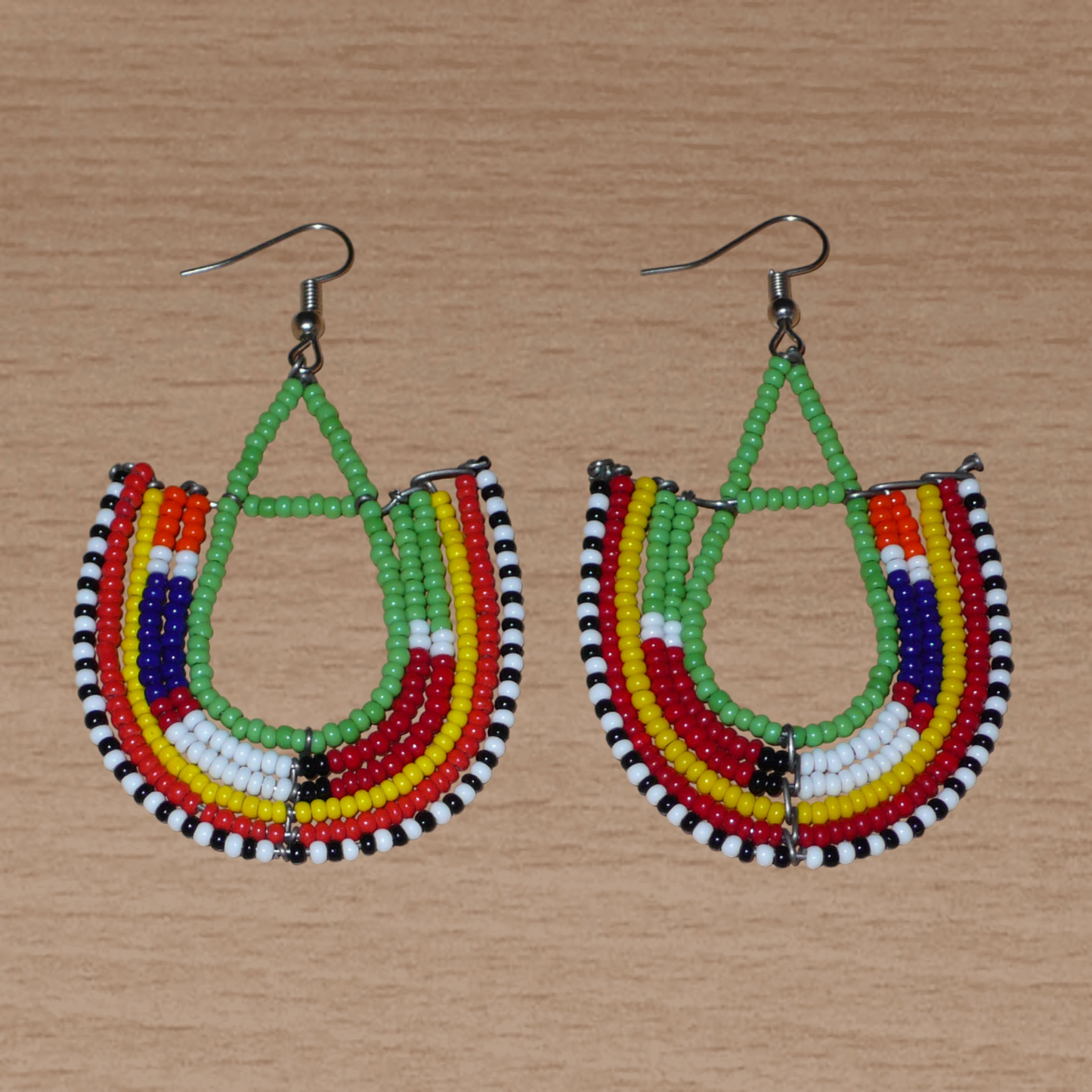 Cette paire de boucles d'oreilles africaines traditionnelles Massai riches en couleurs, de conception artisanale kenyane, apportera une touche tribale à votre look ! Elles se composent de perles de rocaille vertes et multicolores glissées sur des structures géométriques en fils de fer montés en forme d'ancres. Ces boucles d'oreilles mesurent 7.5 cm de long et 4.5 cm de large, et se portent avec des crochets en acier inoxydable sur des oreilles percées.