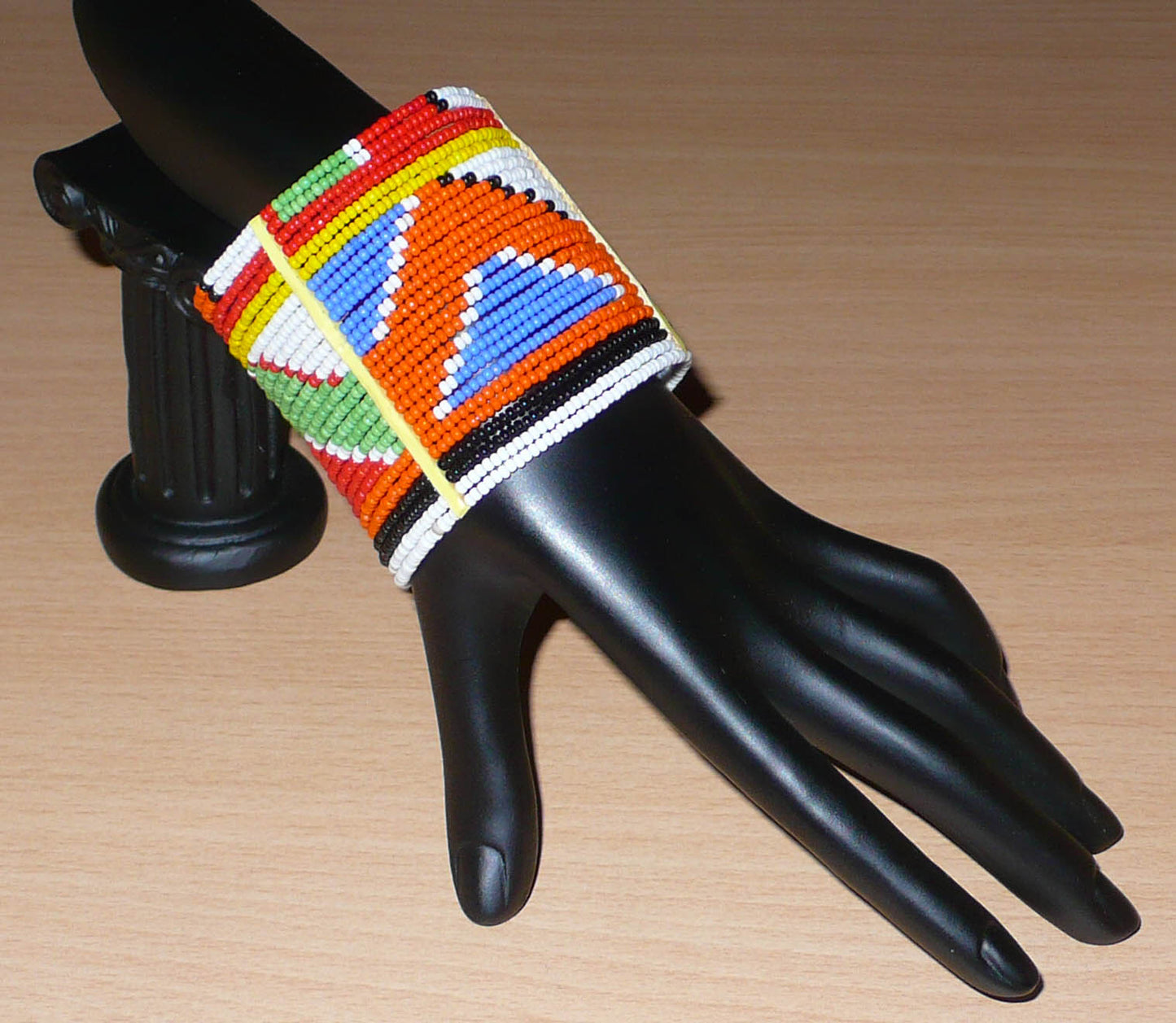 Bracelet africain traditionnel composé de perles de rocaille aux couleurs et motifs ethniques Massai enfilées sur vingt-six rangées de fils de fer fixés sur des charnières en plastique. Il se ferme avec des boutons pressions.