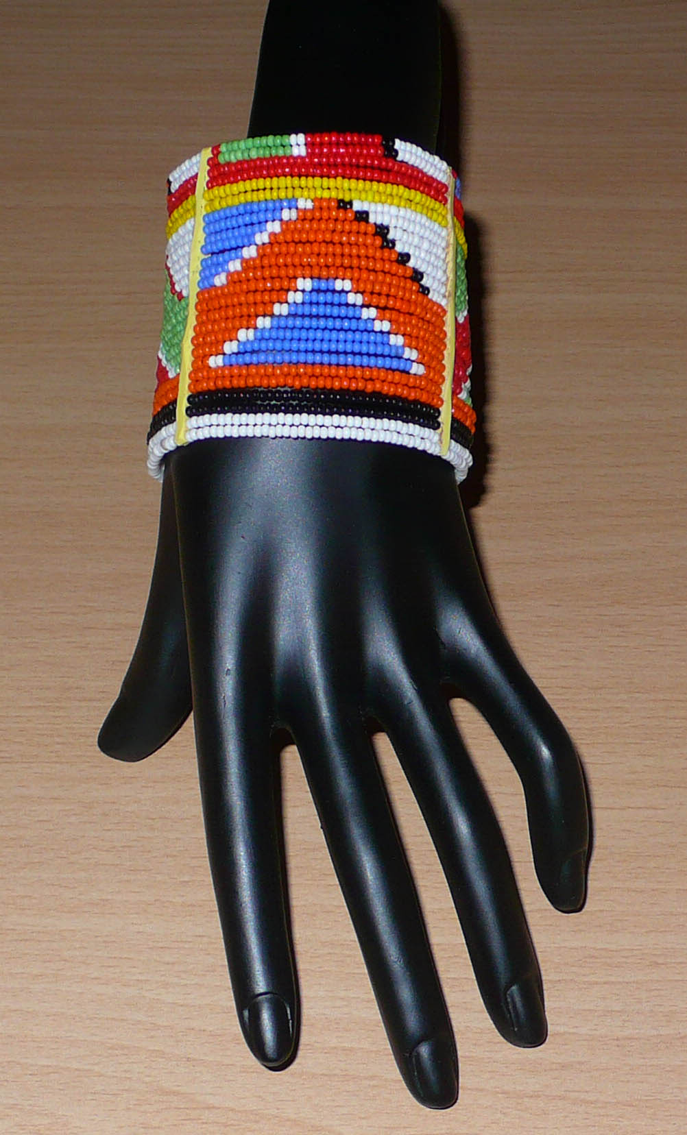 Bracelet africain traditionnel composé de perles de rocaille aux couleurs et motifs ethniques Massai enfilées sur vingt-six rangées de fils de fer fixés sur des charnières en plastique. Il se ferme avec des boutons pressions.
