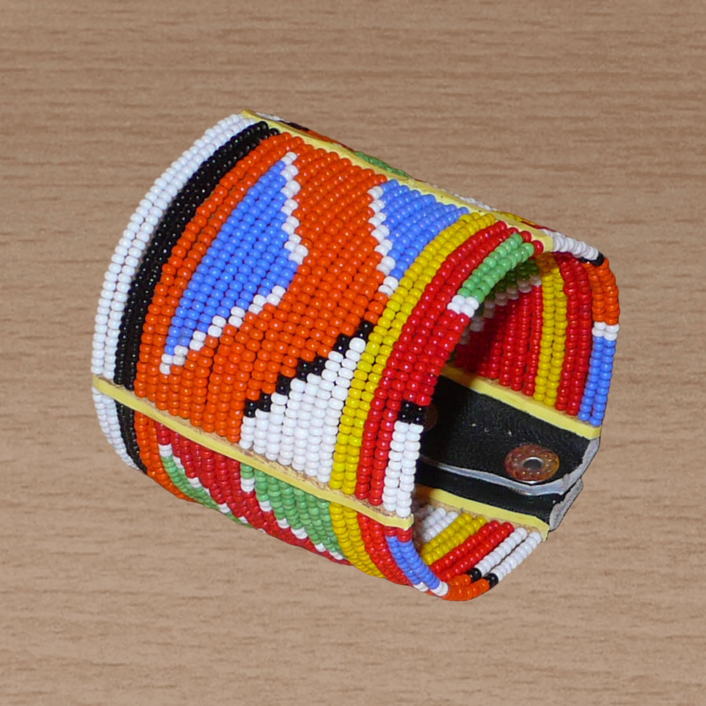 Bracelet africain traditionnel composé de perles de rocaille aux couleurs et motifs ethniques Massai enfilées sur vingt-six rangées de fils de fer fixés sur des charnières en plastique. Il se ferme avec des boutons pressions.
