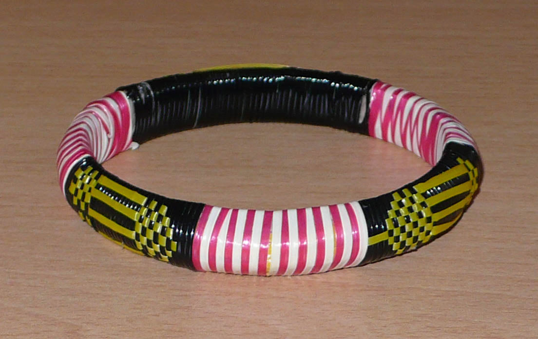 Bracelet africain fabriqué dans une optique eco-responsable avec des matériaux de récupération : il se compose de motifs ethniques tissés à partir de fines bandes de plastique recyclé noir, jaune, rouge et blanc.
