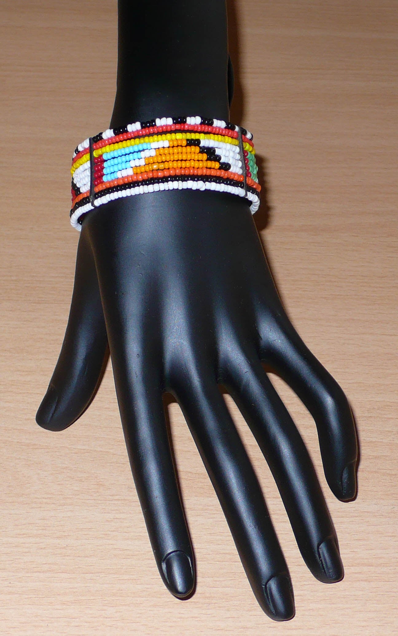 Bracelet africain tribal à motifs géométriques Massai fait de dix rangées de perles de rocaille multicolores enfilées sur des fils de fer fixés sur des charnières en plastique. Le bracelet se ferme avec des crochets.