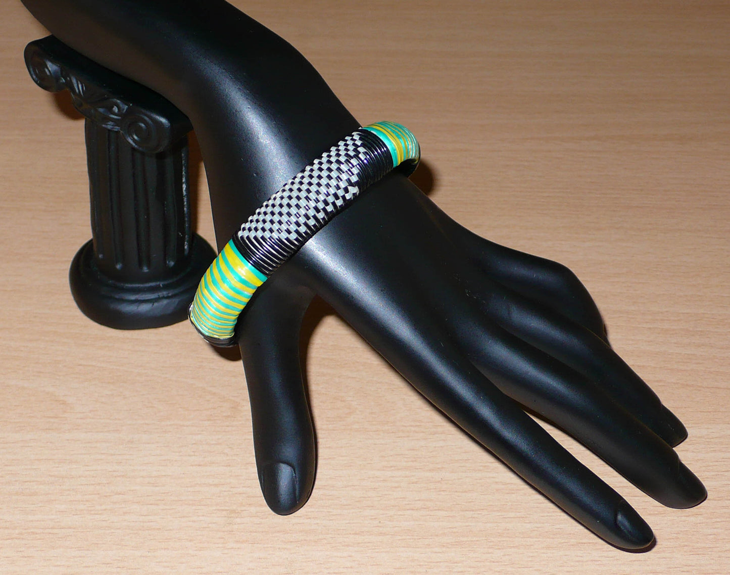 Bracelet africain eco-friendly tressé avec des fines bandes de plastique recyclé noir, blanc, vert et jaune.