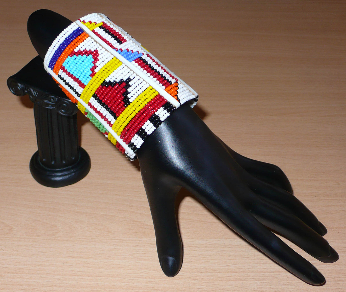 Bracelet africain pour enfant à motifs ethniques traditionnels Massai composé de trente-six rangées de perles de rocaille blanches et multicolores glissées sur des fils de fer fixés sur des charnières en plastique blanc.