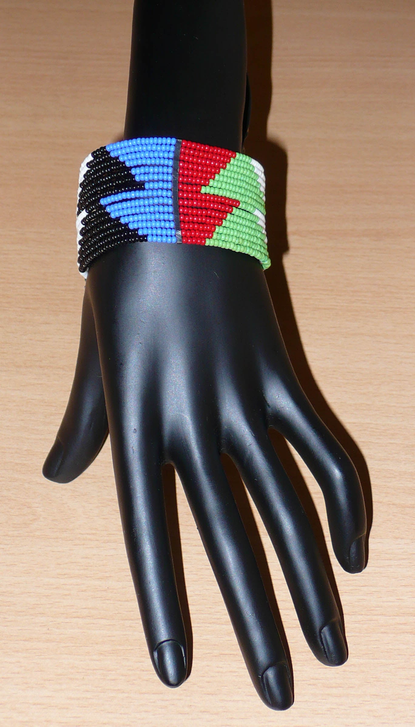 Bracelet africain Massai à motifs ethniques géométriques composé de quatorze rangées de perles de rocaille rouges, bleues, vertes, blanches et noires ; il s'attache avec deux crochets.