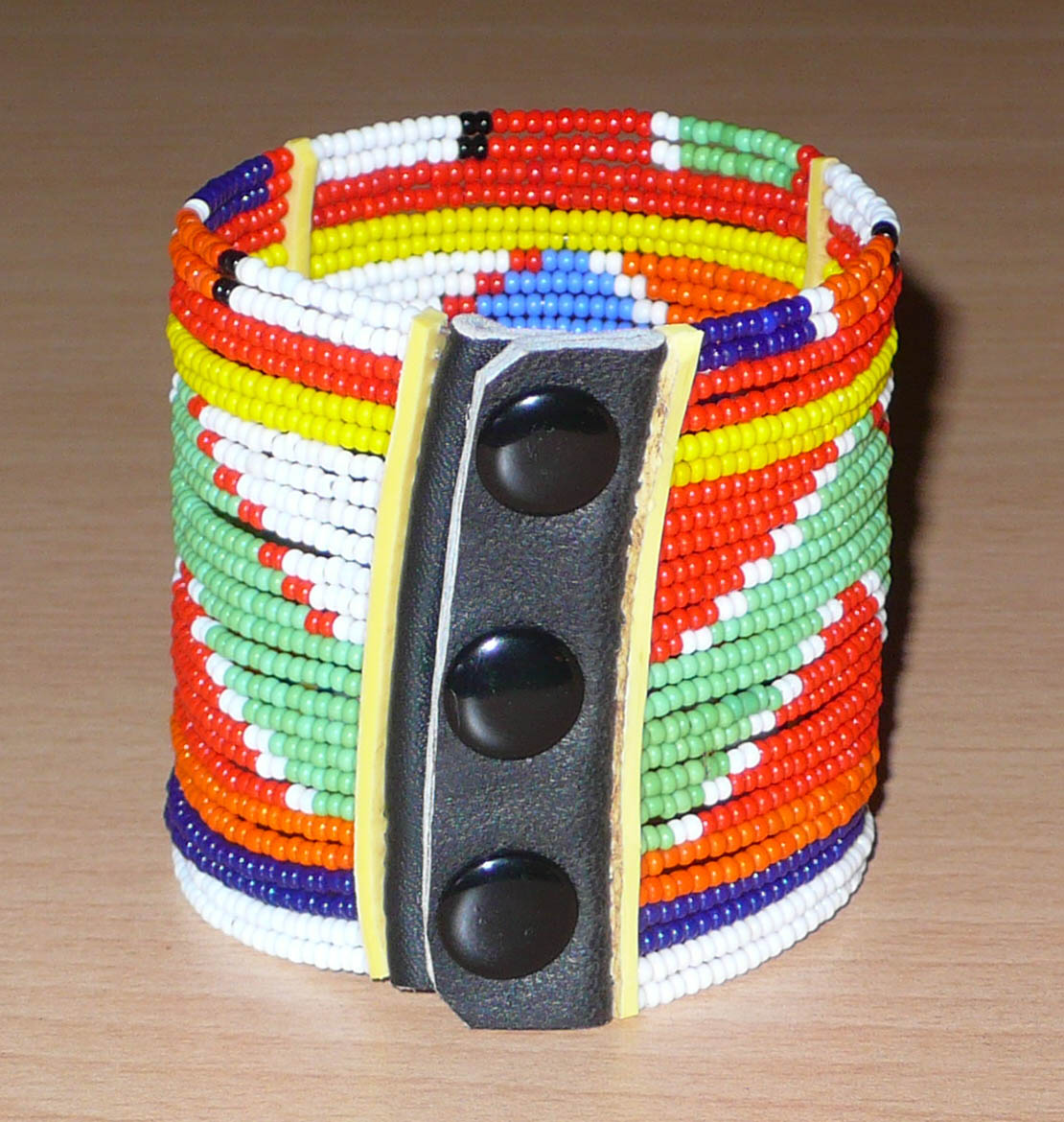 Bracelet africain traditionnel composé de vingt-six rangées de perles multicolores aux couleurs et motifs Massai enfilées sur des fils de fer fixés sur des charnières en plastique. Le bracelet se ferme avec des boutons pressions.