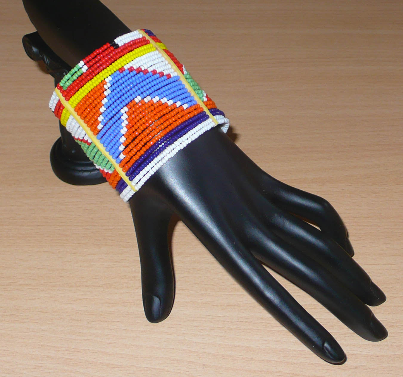 Bracelet africain traditionnel composé de vingt-six rangées de perles multicolores aux couleurs et motifs Massai enfilées sur des fils de fer fixés sur des charnières en plastique. Le bracelet se ferme avec des boutons pressions.