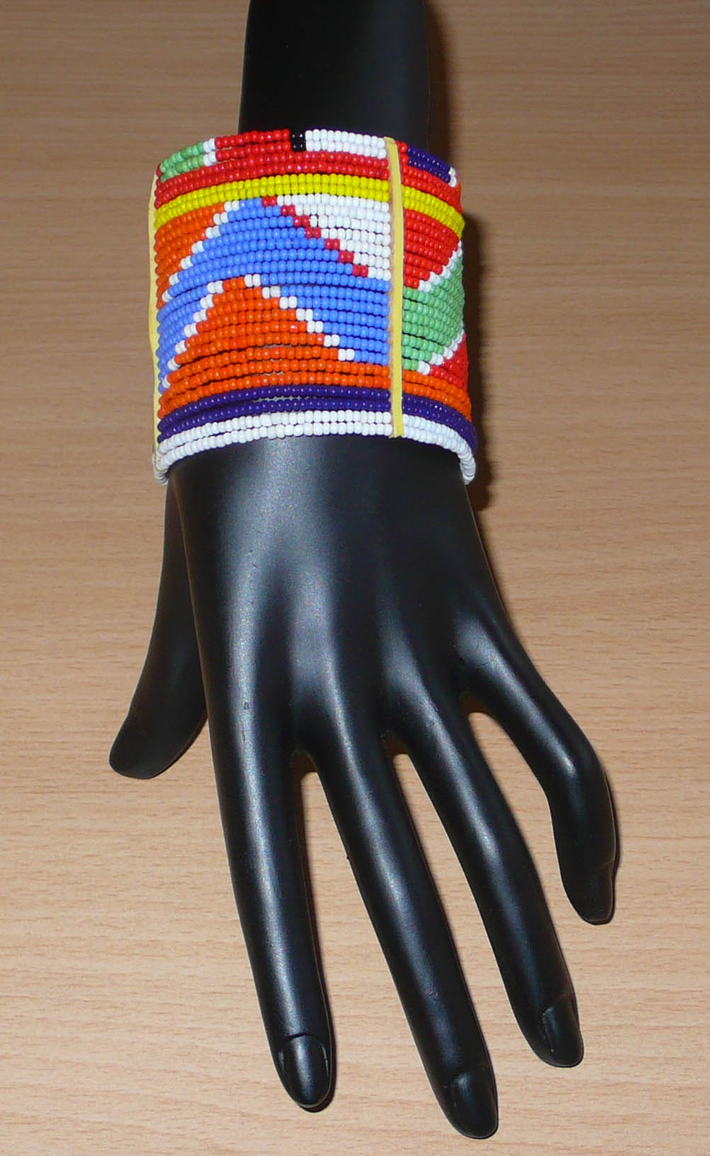 Bracelet africain traditionnel composé de vingt-six rangées de perles multicolores aux couleurs et motifs Massai enfilées sur des fils de fer fixés sur des charnières en plastique. Le bracelet se ferme avec des boutons pressions.