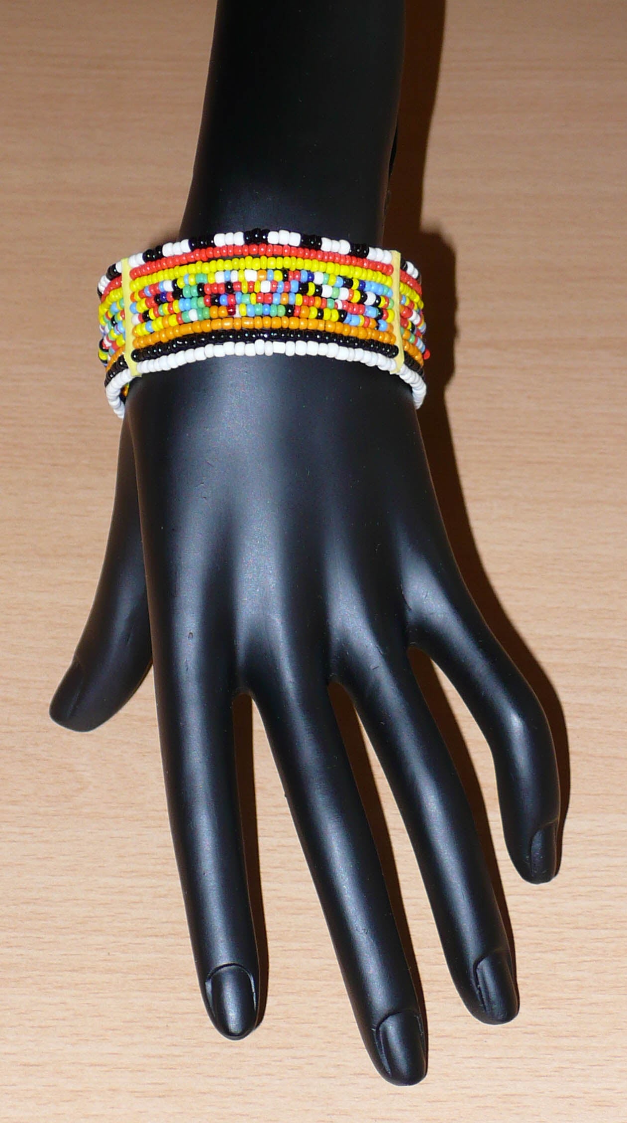 Bracelet africain Massai composé de dix rangées de perles de rocaille multicolores enfilées sur des fils de fer fixés sur des charnières en plastique. Le bracelet se ferme avec deux crochets.
