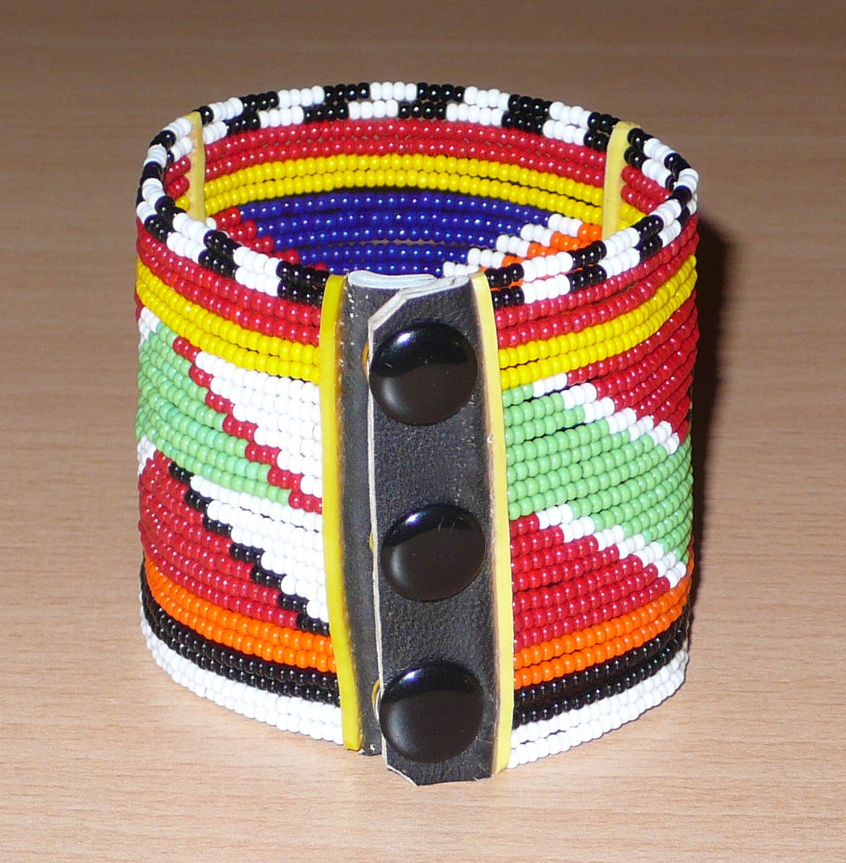 Bracelet africain traditionnel multi-rangs à motifs géométriques Massai composé de perles de rocaille multicolores enfilées sur vingt-six rangées de fils de fer fixés sur des charnières en plastique. Il s'attache avec des boutons pressions.