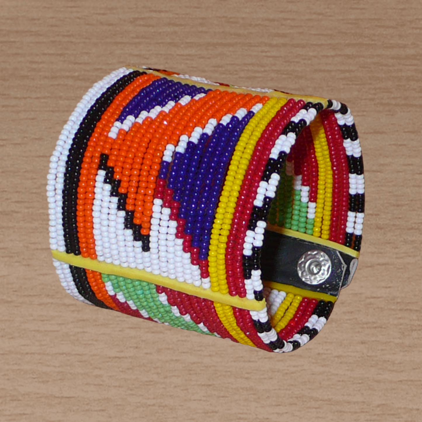 Bracelet africain traditionnel multi-rangs à motifs géométriques Massai composé de perles de rocaille multicolores enfilées sur vingt-six rangées de fils de fer fixés sur des charnières en plastique. Il s'attache avec des boutons pressions.