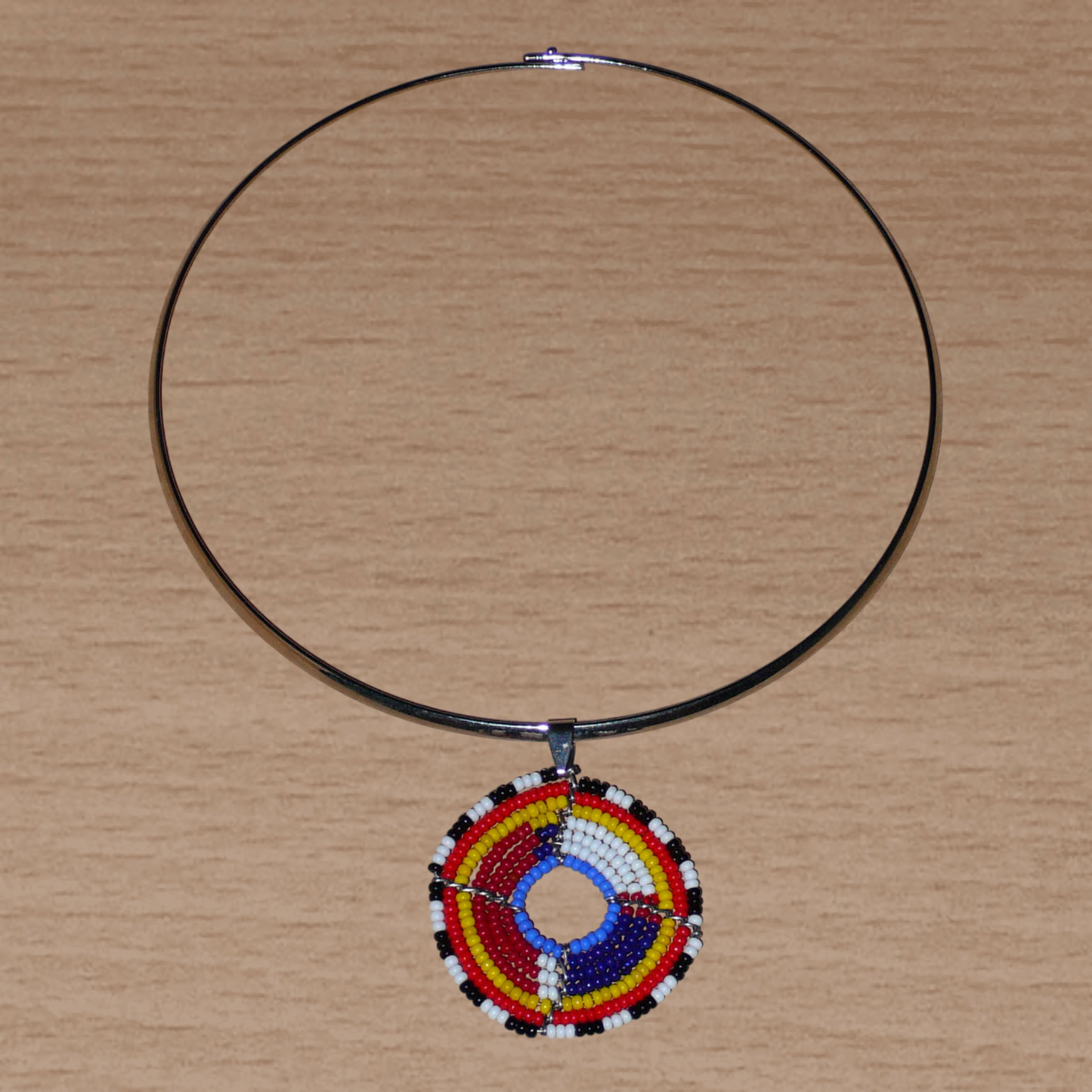 Collier africain composé d'un ras de cou en laiton orné d'un petit médaillon fait d'un tissage de perles de rocaille. Il mesure 18,5 cm de long, la circonférence du ras de cou est de 42,5 cm et son diamètre de 13,5 cm ; le médaillon mesure 4,5 cm de long et de large.