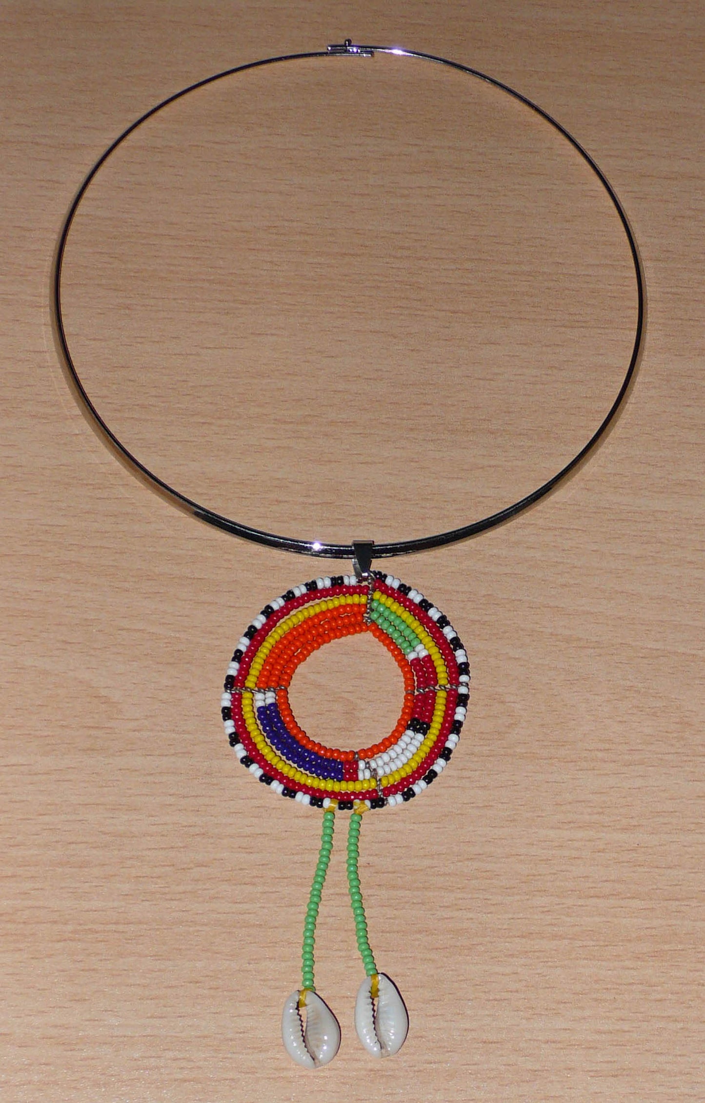 Collier africain se composant d'un ras de cou en laiton orné d'un long pendentif ethnique Massai en perles de rocaille vertes et multicolores et coquillages cauris.